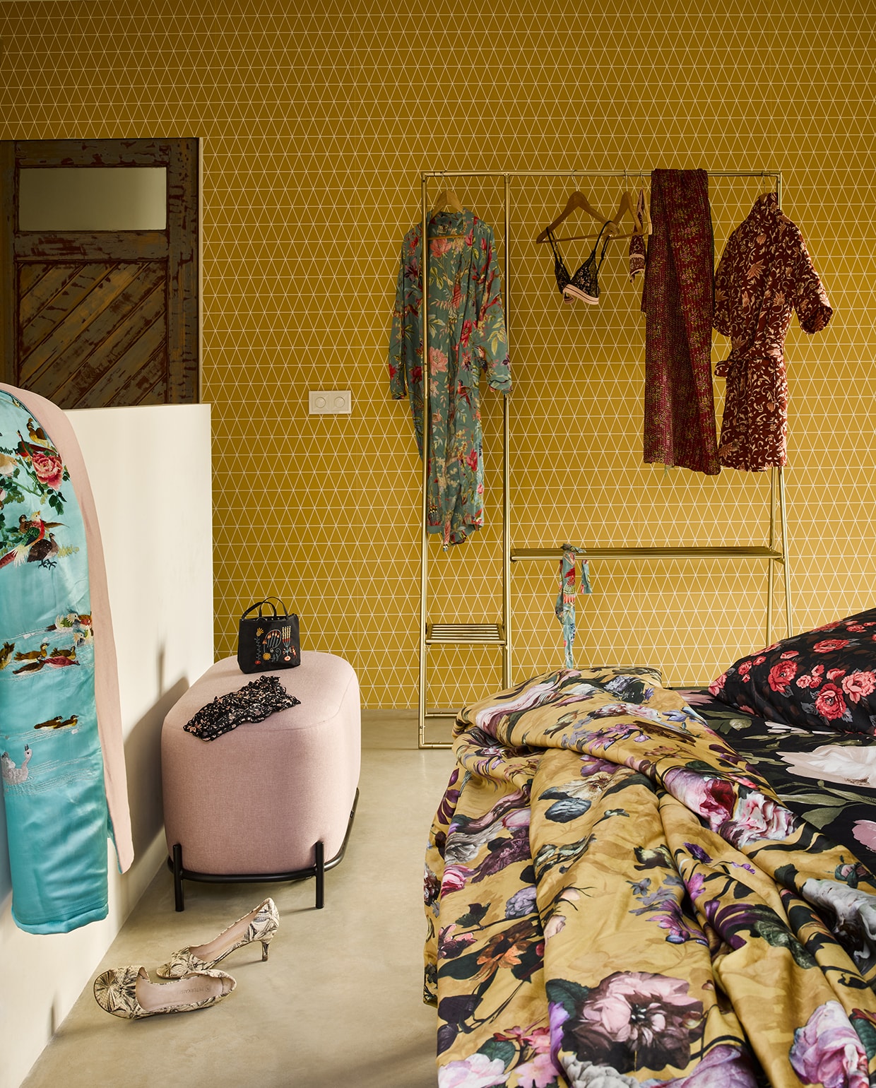 Behang Superfresco Easy v.a. (gamma.nl). Dekbedovertrek Blekfryle, 200×200 cm, dekbedovertrek Backvicker, 200×200 cm (ikea.nl). Gele sprei Fleur van Essenza, 170×135 cm (lxb), kledingrek van hkliving, oudroze poef van hkliving, 45x80x40 cm (hxbxd) (vtwonen.nl). Zijden plaid, zijden sjaal (aan rek) (brechtjeolsthoorn.nl). Blauwe gebloemde kimono, rode gebloemde jas, beha, slip (op poef), tasje (op poef) (maisonnl.com). Schoenen privé.