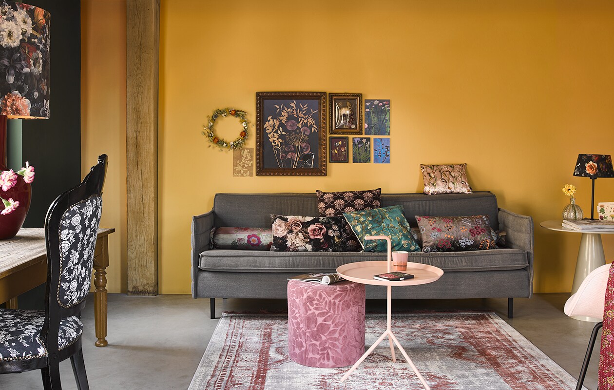 Muurverf Straw van vtwonen (karwei.nl). Bank Jaey, 181x90x76 (bxdxh) v.a. (zuiver.com). Stoel van Loods5 Design, roze bijzettafel met handvat, roze poef, 35 x 45 cm (Øxh), gebloemde lampenkap op lampvoet (loods5.nl). Zijden rolkussens, bruin geborduurd kussen, zijden sjaal (over stoel) (brechtjeolsthoorn.nl). Gebloemd kussen, kussen op rugleuning, groot kussen achter blauw kussen (loods5.nl). Vloerkleed Marvel van Zuiver, 240×170 cm (lxb), bijzettafel van hkliving (vtwonen.nl). Bolvormige vaas met reliëf privé. Aan de wand: krans van droogbloemen, lijsten met droogbloemen groot, middel en klein, gebloemd tasje op tafel (maisonnl.com). Antieke tafel 160 x 70 x 72 cm (lxbxh) (burbri.nl). Gebloemde lampenkap op rode keramische voet (polspotten.nl). Glazen flesje (Waterdrinker). Stoel (hetgoed.nl).
