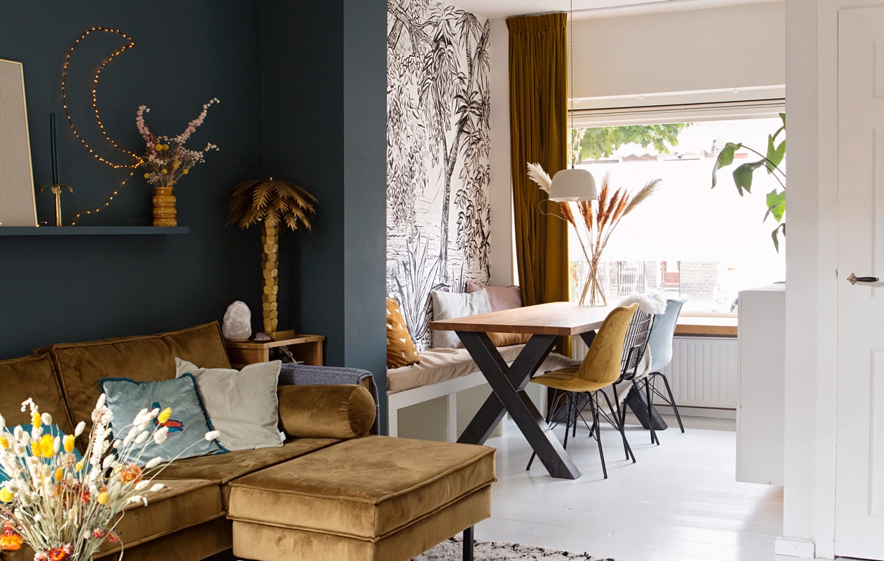 Bank Rodeo van Be Pure Home in honing geel, palmboom lamp hkliving, maanlamp zelfgemaakt, tafelblad en -poot via Marktplaats, gele en blauwe velours stoelen Kick, zwarte metalen stoel vintage, hanglamp SissyBoy, wandplank Ikea, accessoires op wandplank vintage vondsten. vtwonen 04-2020 | fotografie Corine Hoge Bavel-Jansen