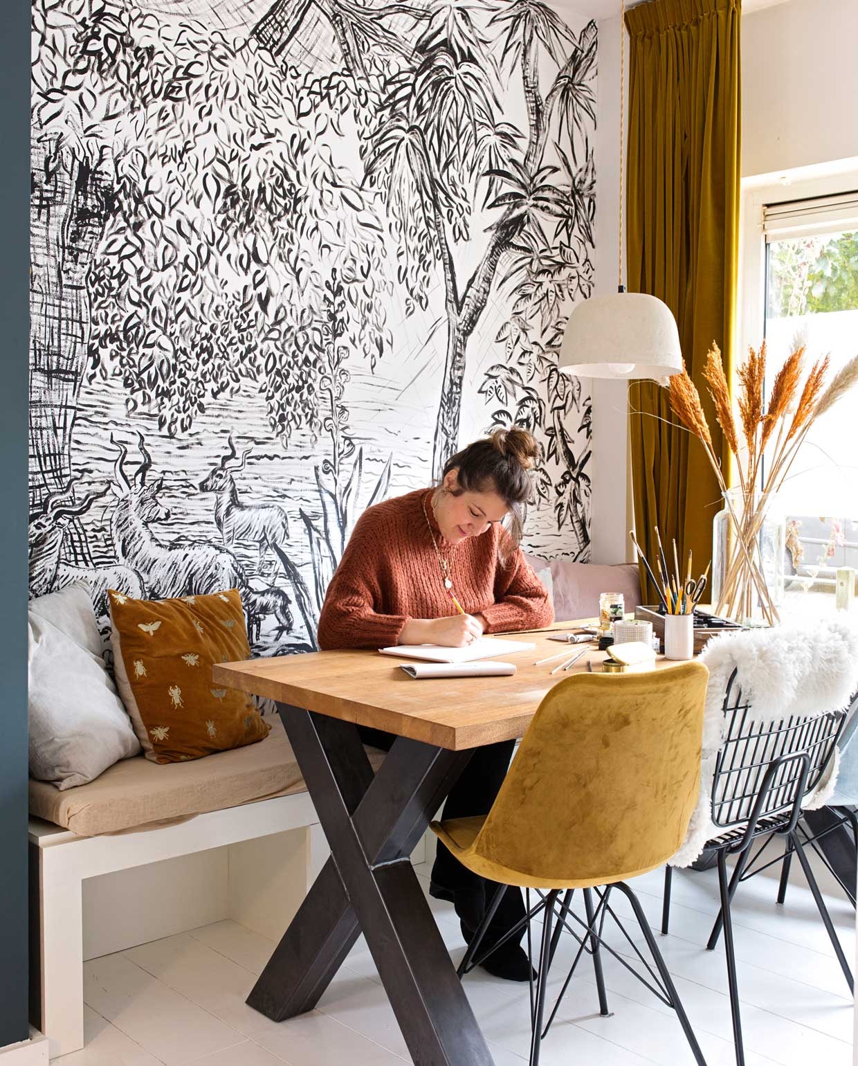 Gordijnen op maat laten maken via Hema. Vaas via een bloemist in de buurt. Nadat Luka soortgelijk behang op een designbeurs in Milaan had gespot dat ver boven haar budget lag, dacht ze: dat kan ik ook. Ze maakte het zelf. Tafel zelfgemaakt met onderdelen van Marktplaats. Kuipstoelen Kick. Draadstoel tweedehands. Fluwelen gordijnen Hema. Lamp en kussenhoes met bijen Sissy-Boy. Roze kussenhoes H&amp;M. Grijze kussenhoezen Loods 5. Bank zelf op maat gemaakt. vtwonen 04-2020 | fotografie Corine Hoge Bavel-Jansen