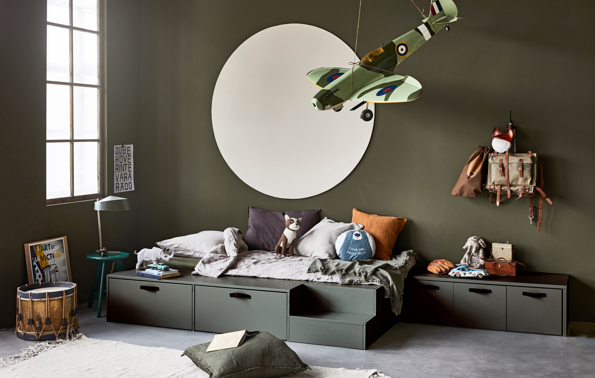 Ladenbed Stage van geschuurd grenen in kleur Soap, 35x204x131 cm (hxbxd), inclusief kast met 2 laden en trapje, exclusief matras (80×200 cm). Kistbank Stage van geschuurd grenen in kleur Soap, 36x120x50 cm (hxbxd). M.m.v. hm.com (linnen dekbedovertrekset, rond kussen beer, hond, zand en okergeel kussen, bruin tasje), wildschut-antiques.com (antiek vliegtuig, trommel), neeflouis.nl (bureaulamp, kruk) vtwonen.nl (vloerkleed van HKliving, donkerbruin kussen van vtwonen), zarahome.nl (groen sprei, linnen kussen), karwei.nl (muurverf camouflage, muurverf flax in stip). Overig privébezit. styling Cleo Scheulderman | fotografie Jeroen van der Spek | studio en decorbouw Milo Kol