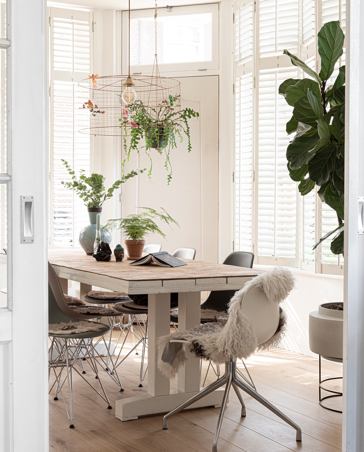 Eettafel gemaakt door Heleen, met een kurken plaat van Kurkwinkel.nl. Lamp Demi-Grande Volière van Mathieu Challières via Vintage Room. Stoelen Vitra. Plantenstandaard Bolia. De vaas op tafel is een erfstuk. Beeld Moeder met kind gemaakt door een vriendin van Heleens moeder, het andere beeld werd meegenomen van Bali. Vloer De Houtfabriek. Schapenvacht Karwei. Schapenvachtjes op stoelen zelf op maat geknipt.
