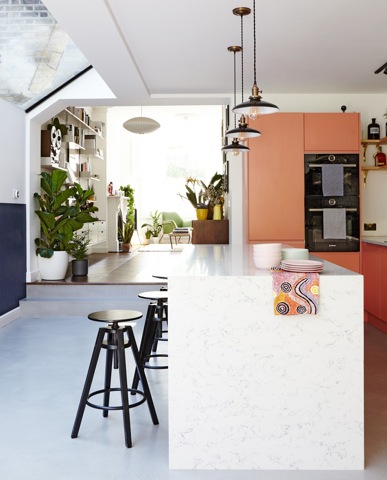 Een verhoging scheidt de woonkamer van de keuken. De zwarte barkrukken Dalfred van Ikea contrasteren met het strakke, op maat gemaakte keukenmeubel uit Silestone kwarts.