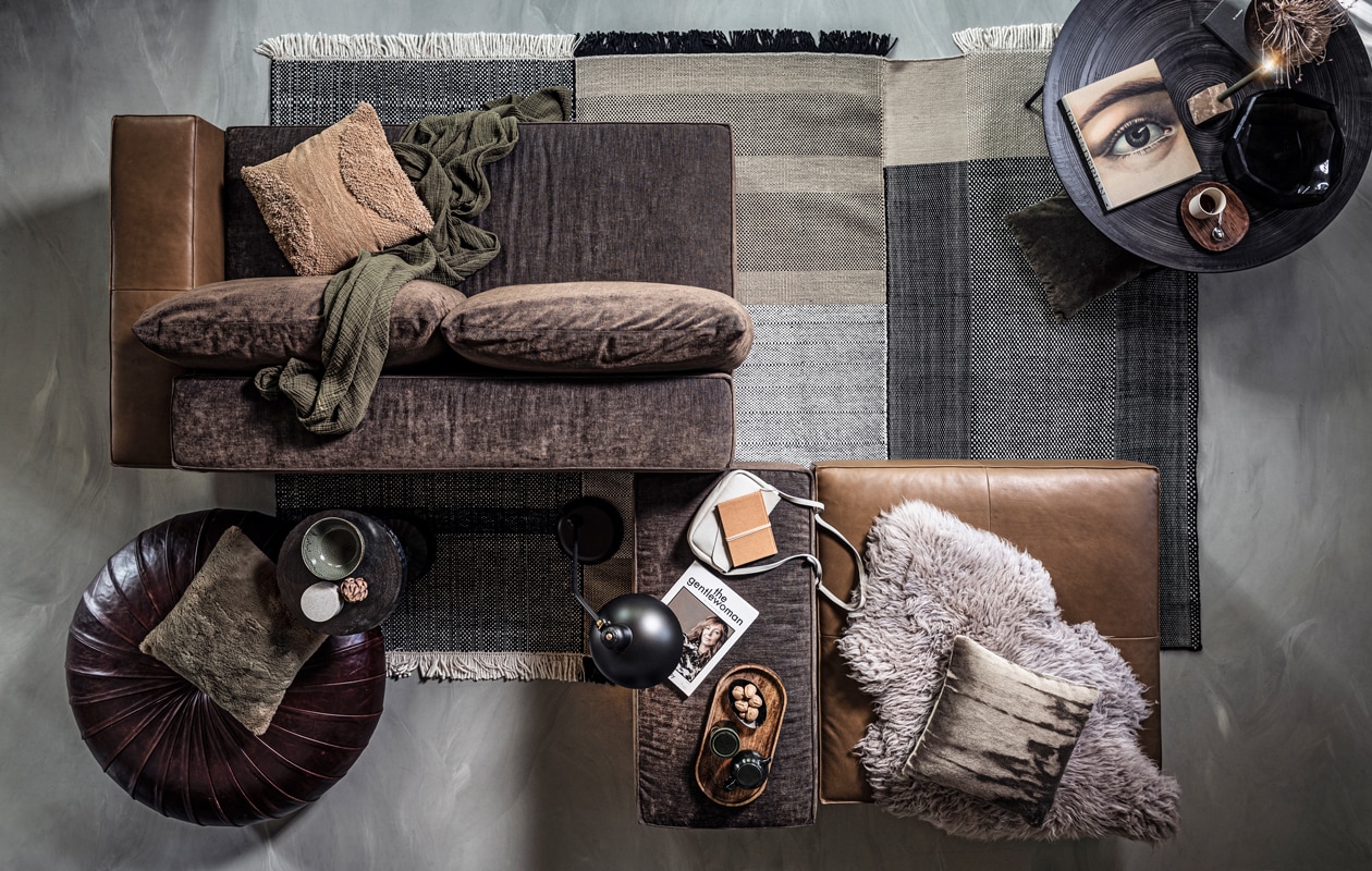 Modulebank, vloerkleed, ronde salontafel, ronde glazen schaal met geometrische vlakken (homestede.nl). Beige kussen met textuurprint, groen kussen met zachte vacht (zarahome.com). Groene plaid, marmeren blok- kandelaar (loods5.nl). Ronde bruin leren poef, beige kussen met vleug (covanderhorst.nl). Ronde metalen bijzettafel op smalle poot (polspotten.nl). Groene kom, groene stenen pot met deksel (thingsilikethingsilove.com). Marmeren pot met deksel, ovalen houten dienblad, houten schotel, gebroken witte mok (hm.com). Zwarte vloerlamp (coosdewitwonen.nl). Zachtgrijs leren tasje, okergeel notitieboekje, groen notitieboek (klevering.nl). Schapenvacht (polspotten.nl). Overig privébezit.