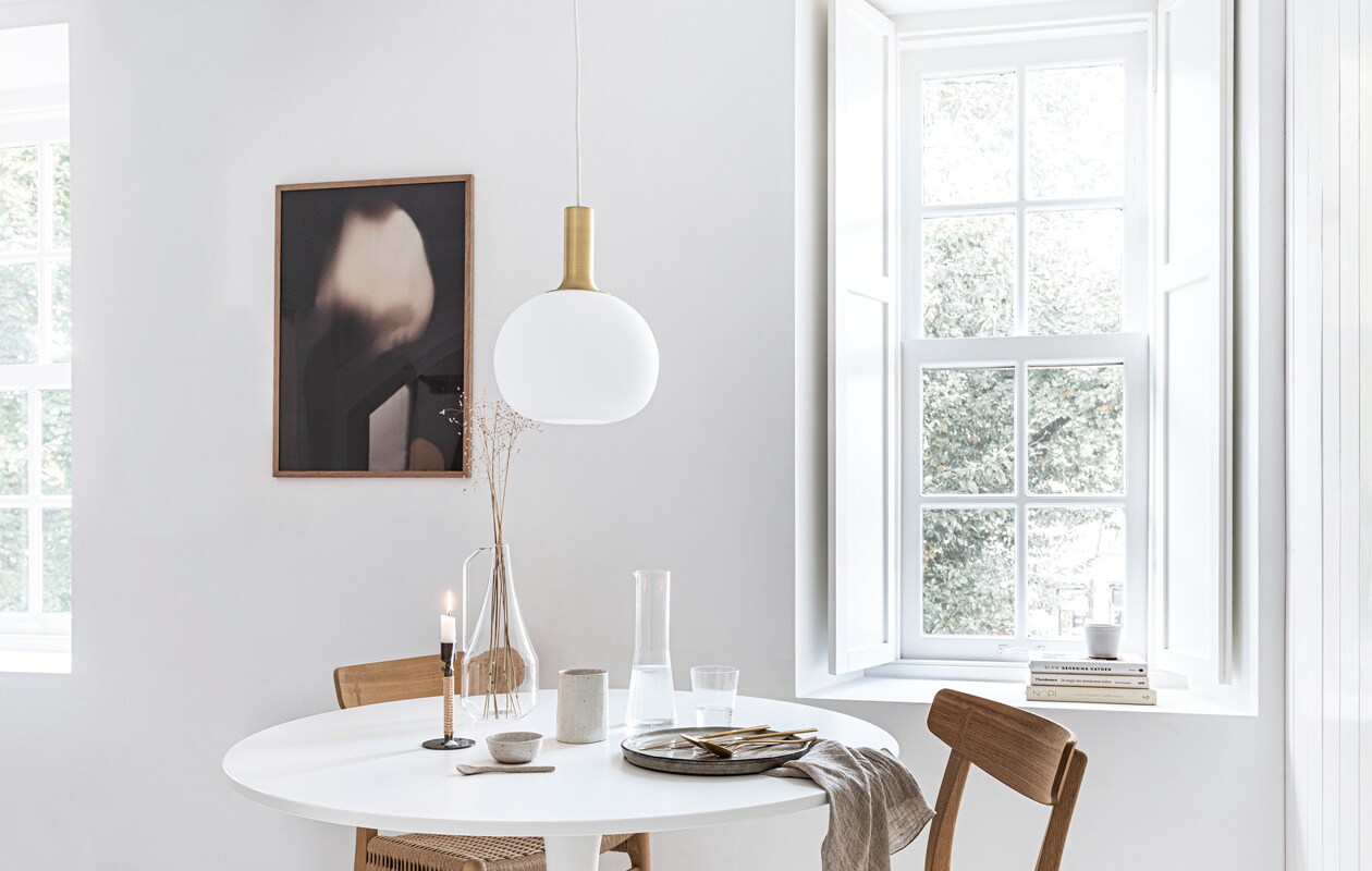 Art print van Gurilla, 50×70 cm, eikenhouten frame, 50×70 cm (theposterclub.com). Hanglamp Alton 25 van Nordlux, groen dinerbord uit de Artisan collectie van Salt &amp; Pepper, Ø 26,5 cm, gouden bestek van Amefa, theedoek uit de vtwonen collectie, 60×60 cm (vtwonen.nl). Witte ronde eettafel Docksta (ikea.nl). Eikenhouten eetkamerstoel met gevlochten zitting CH23 van Carl Hansen &amp; Søn (coosdewitwonen.nl). Messing kandelaar omwikkeld met rotan Duca (menu.as). Glazen karaf met handvat, drinkglas met ribbels, kegelvormige glazen kan met ribbels, beker aardewerk (zarahome.com). Overig privébezit.