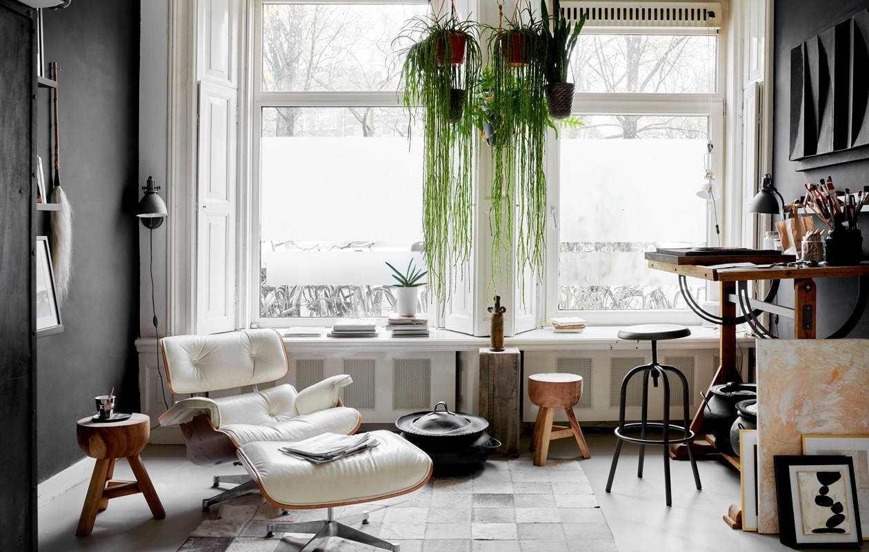 Het atelier in de voorkamer met lounge chair en ottoman van Eames voor Vitra. Tekentafel, krukken en slagersrek Marktplaats. Lamp Serge Mouille. Leren karpet overgenomen van een vriend. Mand uit Marokko. Sokkel van een markt, de vaas erop is een reissouvenir. NEE | vtwonen 2-2020 | fotografie Wilma Custers/features &amp; more | tekst Chris Muyres