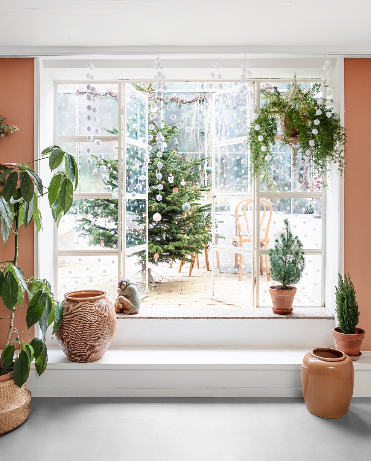 De keuken en eetkamer bevinden zich in het souterrain van het huis en geven toegang tot de serre waar het gezin het hele jaar door te vinden is. De overgang tussen het eetgedeelte en de orangerie is weelderig gedecoreerd met groene planten (hellonature.dk). Op de muur kleur Terra di Siena van Flügger. Op de glazen deuren heeft Rikke een decoratie van sneeuwvlokken aangebracht. vtwonen 13-2019 | styling Rikke Graff Juel | fotografie Christina Kayser O.