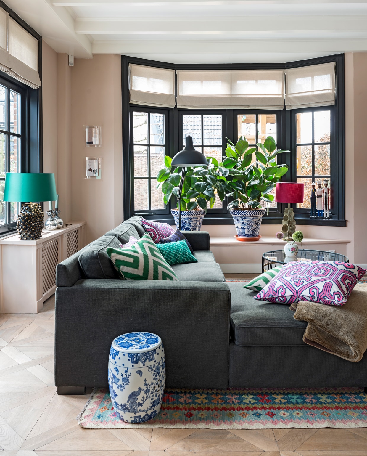 De bank en staande lamp komen uit een woonwinkel die niet meer bestaat. Lamp met roze kap Eveline Interieur. Kussens van Eveline Interieur, Elitis en Mariska Meijers. Plaid herkomst onbekend. Kleed groothandel. Chinese pot stond in de kelder van Diederiks ouders. Salontafel Paul Lelieveld. Potje groothandel. De beelden op de vensterbank komen uit Afrika. Plantenpotten uit Spanje, verkrijgbaar bij Studio Sophie. Lijsten aan de muur van HK Living. De zilveren kandelaars waren een cadeau van Sophies ouders. Muurverf Setting Plaster van Farrow &amp; Ball. Vouwgordijnen zaten al in het huis. Kozijnen geschilderd in kleur Ral 9004. vtwonen special binnenkijken 12-2019 | styling Lindividu | fotografie Stan Koolen, CocoFeatures