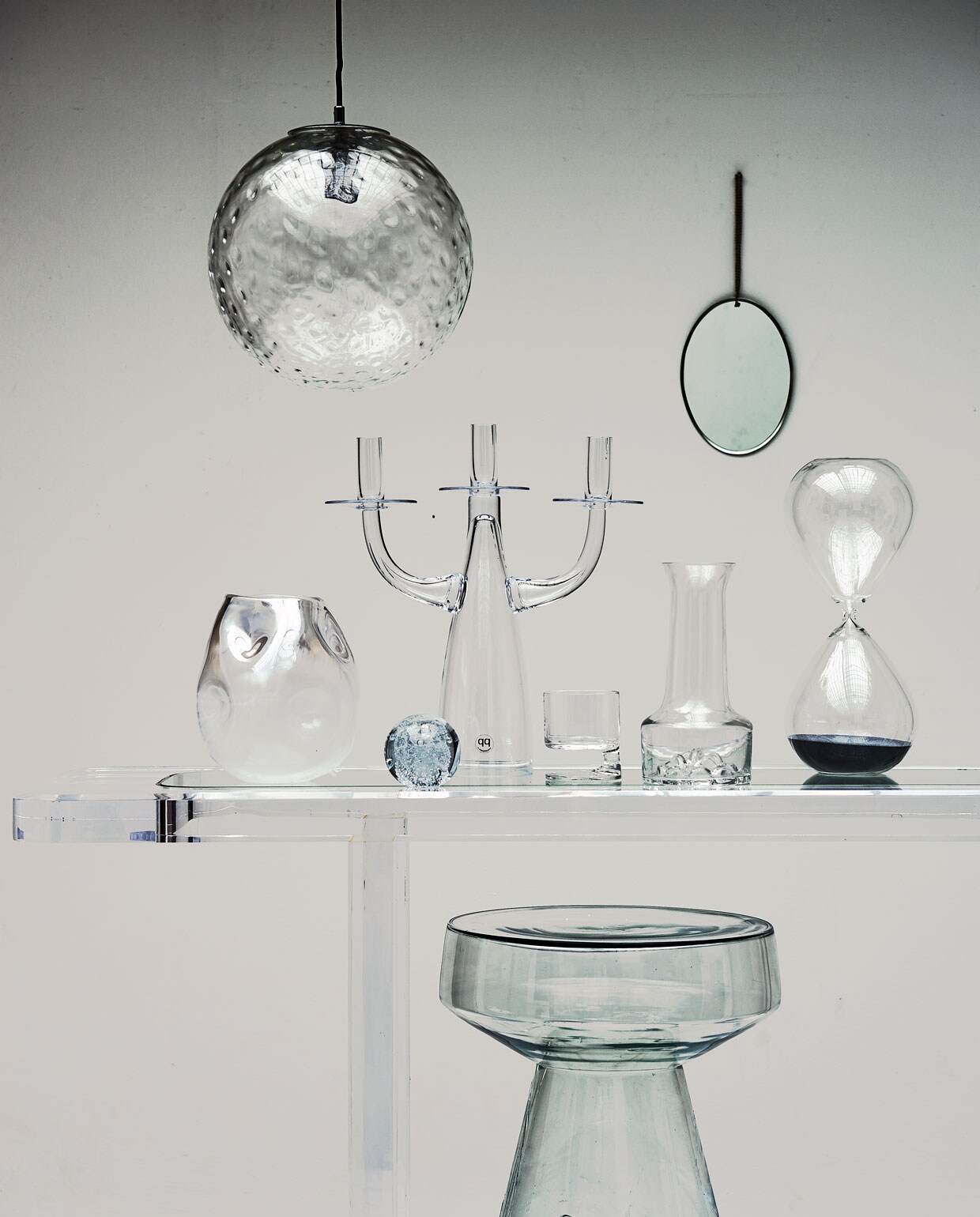 Plexiglas tafel, hanglamp, whiskyglas van Joe Colombo, karaf (neeflouis.nl). Vaas met deuk, 3-armige kandelaar, zandloper (polspotten.nl). Presse-papier, glazen bijzettafel (hkliving.nl). Spiegel (weldaad.com).