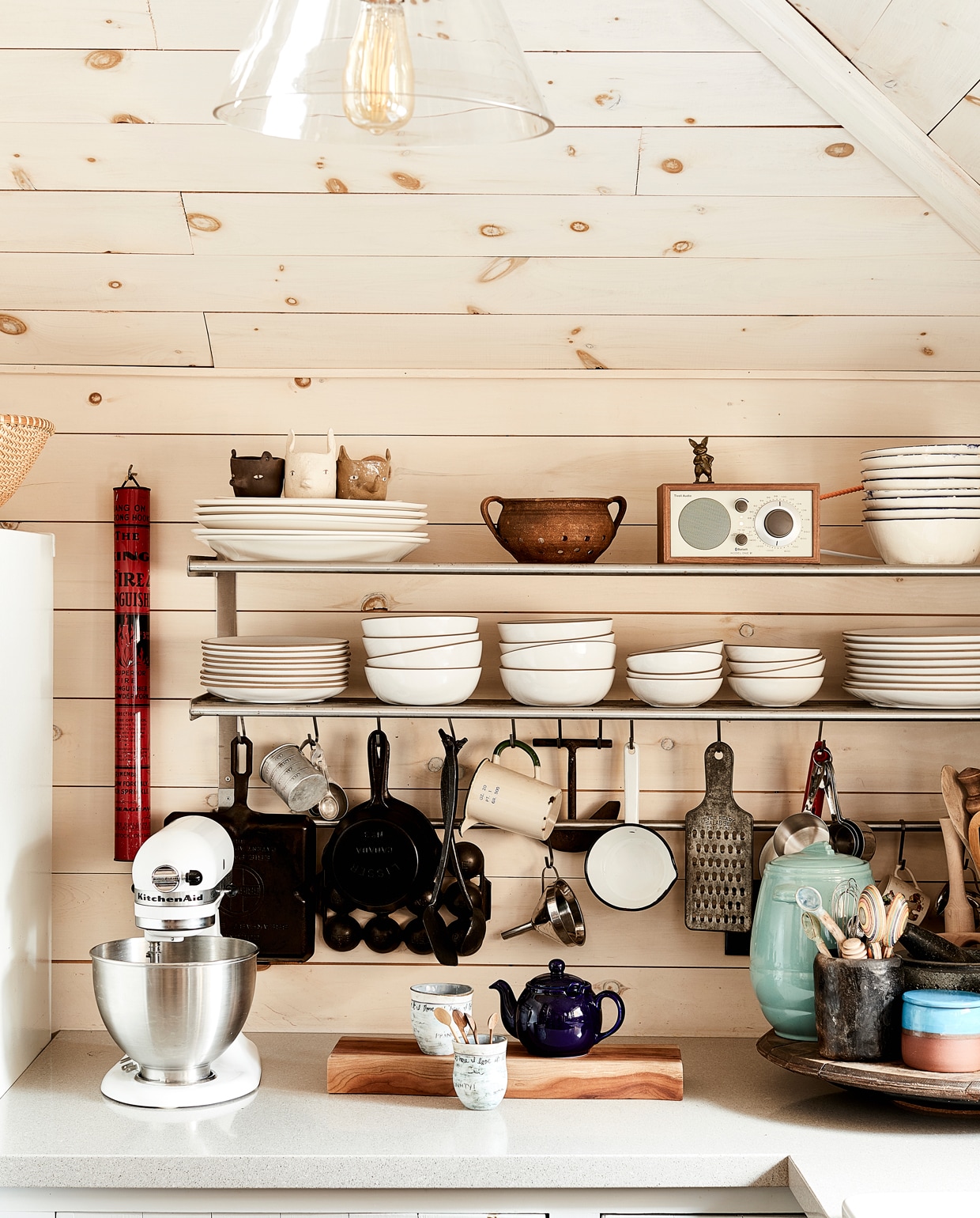 Wit servies en hier en daar details in zwart en roestvrijstaal geeft die rustige Scandinavische woonsfeer. De drie keramische mokken links boven op het bordenrek zijn gemaakt door Sarah Burwash. Borden en schalen met terracotta rand van Heath Ceramics. Soortgelijk rvs wandrek Grundtal van Ikea. Komgreepjes voor lades zijn in deze stijl te koop bij Weijntjes.
