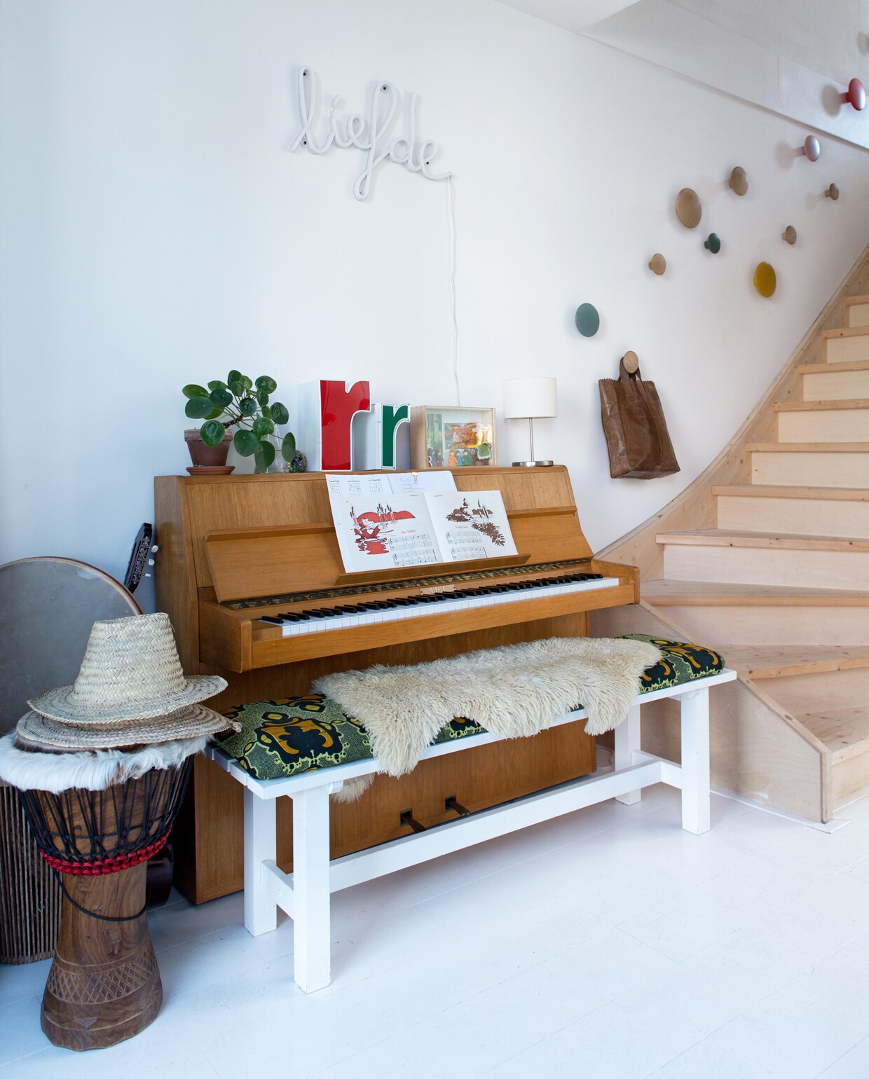 Tussen de voordeur en de trap staat een piano die van Michiels oma was. Bankje Ikea, kussen zelfgemaakt. Gekleurde doosletters Westside Den Bosch. Neon-lamp Liefde van Zilverblauw. Aan de muur The Dots van Muuto die dienstdoen als trapleuning. vtwonen 12 binnenkijken special 2019 | Styling Jet van der Graaf | Fotografie Trui Heinhuis