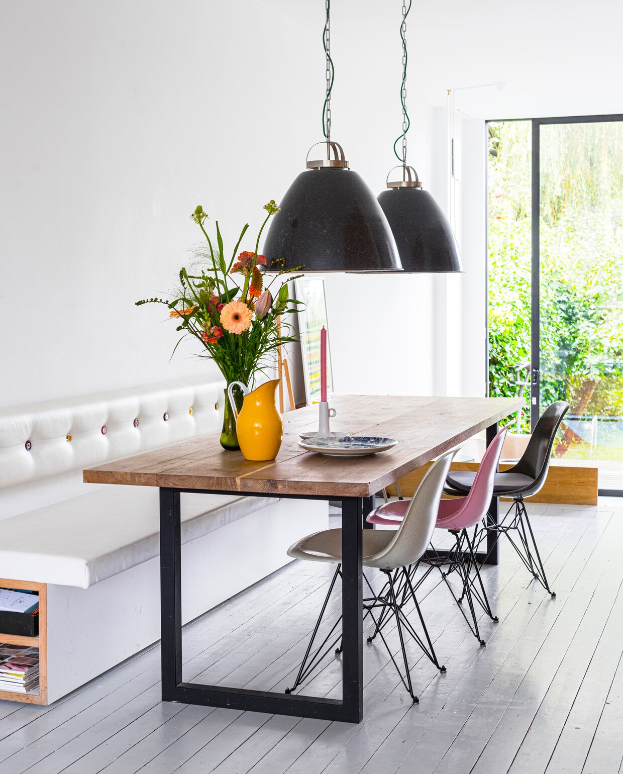 Boven de tafel vintage fabriekslampen van Vaen vintage design (Utrecht), kinderstoeltje en zwart krukje van Ikea, glasfiber kuipstoelen van Eames via Modernica, emaillen schenkkan van handiggoed.nl, vaas van Pol’s Potten. Eettafel via Depot Rotterdam.