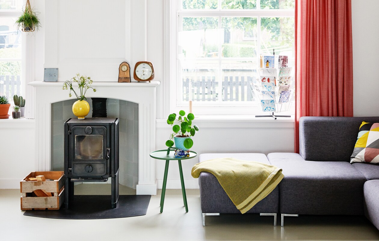 Bank Karwei. Deken Muuto, kussens Ferm Living, gele vaas Kahler, alles via Nio &amp; Elva. Sidetable Montis door Lambie &amp; Van Hengel, erop cadeau gekregen oude tinnen autootjes. Vintage kaartenrek van antiquariaat. Houtkagel Morse. Houten Klokken en blauw bloempotje zijn familieerfstukken, tegeltjes Storytiles. Plant Pilea Peperomioides. Vloer polyutheraan in kleur RAL7044 door Hoogeveen Vloertechniek. Gordijnen Post Woonadvies.