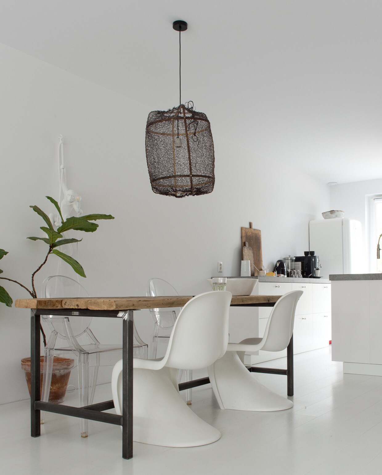 De witte Verner Panton stoelen en de Ghost Chairs van Kartell vormen een mooi contrast met de ruwe houten eettafel van Barn9 Woodconcepts. Lamp Ay Illuminate van loftloft.nl. Broodplanken uit Frankrijk. Vloer van Strongfloor. De keuken ontwierp Dennis zelf, de lades zijn van Ikea. vtwonen 12 binnenkijken special 2019 | Styling Wilma Custers (Features &amp; More), Rozmeen Koornneef | Fotografie Trui Heinhuis