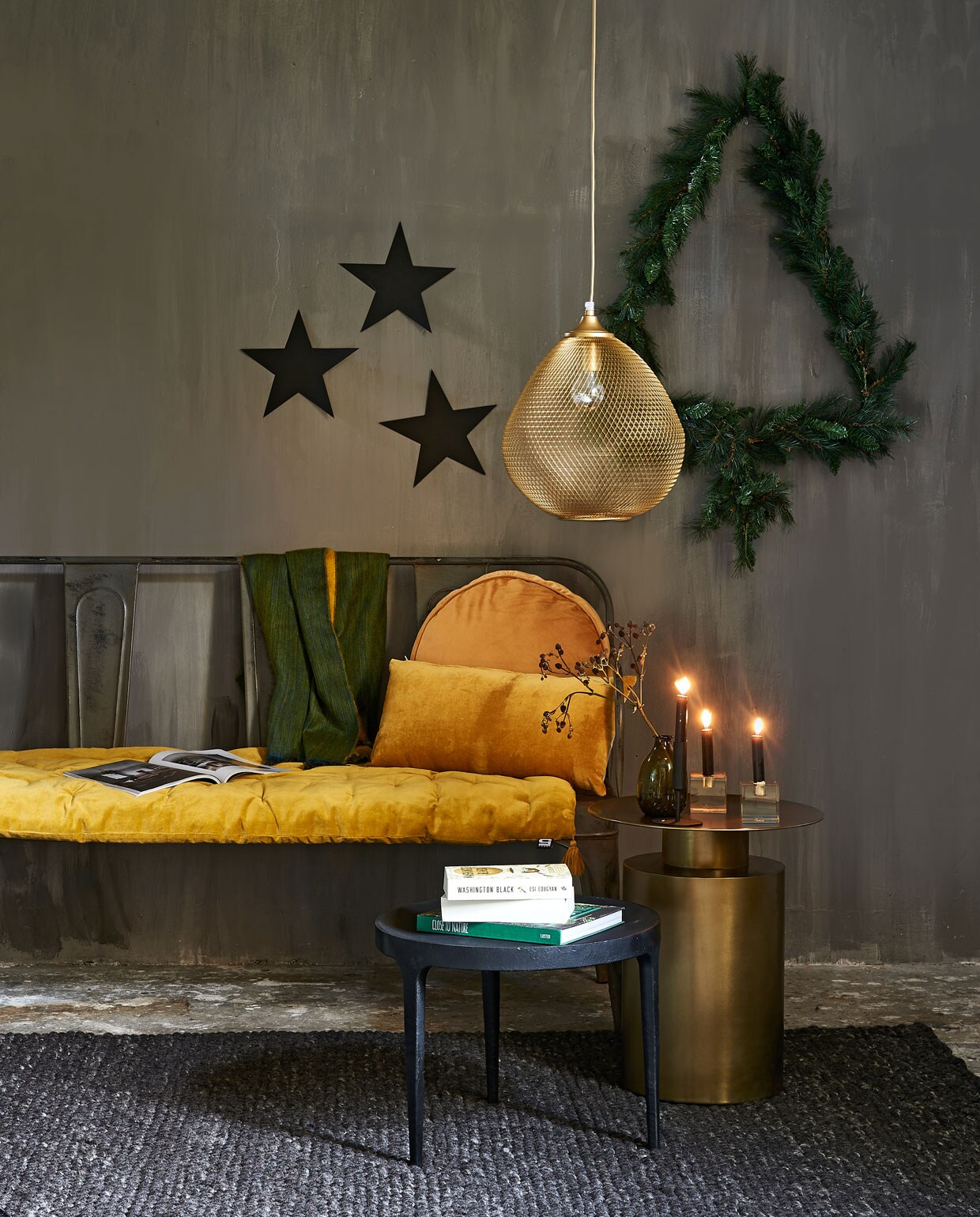 Metalen bank, groen vaasje (weldaad.com). Lamp (bodilson.com). Koperen tafel van Loods 5 Design,zwart tafeltje van Loods 5 Design (loods5.nl). Kerstslinger waarmee de kerstboom op de wand is gemaakt (rivieramaison.nl). Geel fluwelen kussen op bank, rechthoekig kussen, rond kussen, groen-gele sjaal (loods5.nl). Vloerkleed Hjorthede, 170×240 cm (ikea.nl). Amberkleurige kristallen kandelaar vierkant (hkliving.nl). Sterren zelfgemaakt. Vaasje privébezit.