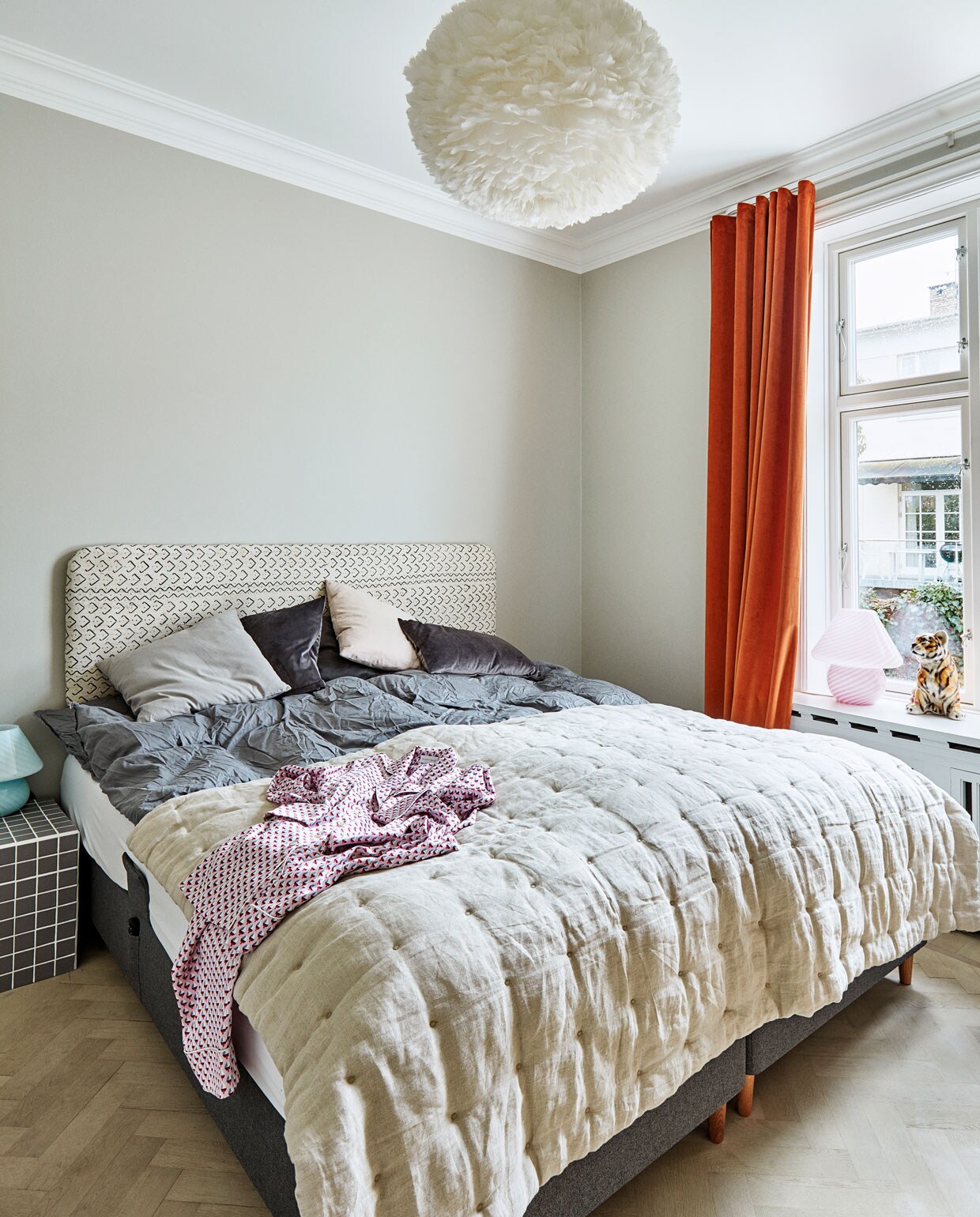 De doorgestikte plaid en kussens zijn van &amp;Drape, net als alle gordijnen in huis. Het bedhoofd en nachttafeltje zijn zelfgemaakt. Hanglamp van Vitra.