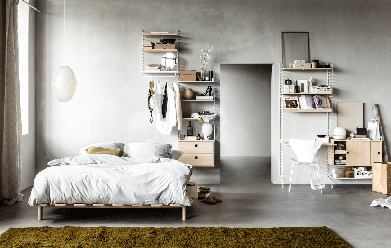 Wandsysteem met witte draadstalen panelen en planken, deuren en werkblad in kleur Ash, (stringfurniture.com). Muurverf kleur North, (bauwerkcolour.com). Vloer Novilon kleur Beton van vtwonen, 200 cm of 400 cm breed, exclusief installeren (vtwonen.nl/vtwonen-collectie). Gordijn Dazer van Kinnasand, 320 cm hoog, witte houten vlinderstoel ronde houten opberger met deksel (coosdewitwonen.nl). Parelmoeren hanglamp, ronde spiegel op eikenhouten poot, canvas tas, bruin flesje olie, eikenhouten lijst, doosjes met knoopjessluiting, plastic kratten, witte kartonnen opbergers, zachtgrijze leren tas met bruin leren koord (letoile.store). Massief beukenhouten bed Modest (loof.nl). Dekbedovertrek met bijpassende slopen van percal katoen in kleur Misty Grey (yumeko.nl). Sierkussen, raffia instappers (zarahome.com). Okergeel berberkleed, verkrijgbaar in elke maat en kleur, 220×340 cm (lxb) (paullelieveld.com). Zwarte ovale marmeren schaal op poten van Ferm Living, grijze glazen karaf van Ferm Living, tafellamp met grijze betonnen poot van Menu, tafellamp met gebroken wit onderstel van Menu (vtwonen.nl). Zwart houten object in cilindervorm zwart houten object in puntvorm, zwart houten opbergschaaltje (loods5.nl). Metalen brillenkoker, grijze fluwelen toilettas met gele kwast (maisonnl.com). Overig privébezit.