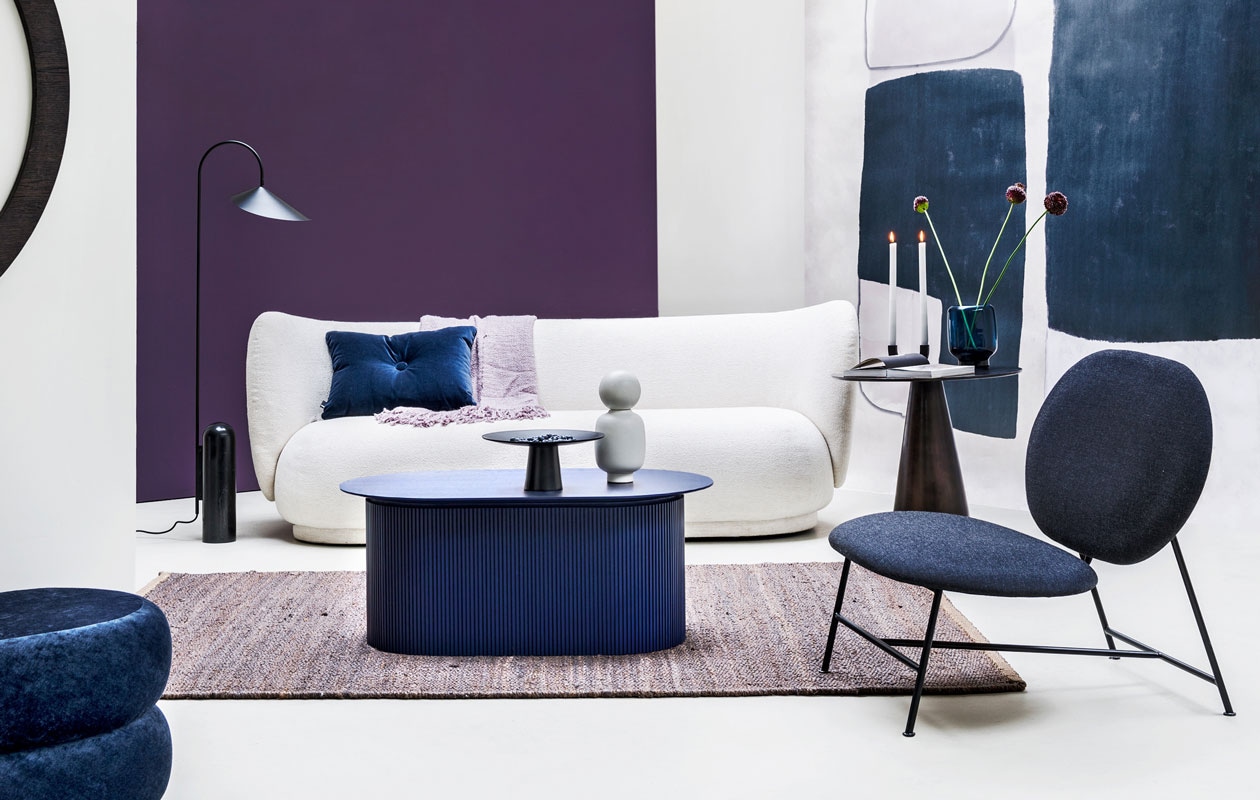 Paarse muurverf Moorland van vtwonen, (karwei.nl). Behang uit collectie Wallpower, 3×3 m (eijffinger.com). Bank Rico 3 met bouclé bekleding, 210×78,5×79 cm (lxbxh), blauwe salontafel, ovale poef van blauw fluweel, lamp met stenen voet (fermliving.com). Fauteuil van Northern, 80x78x73 cm (lxbxh) (goeds.nl). Metalen tafeltje, 60×56 cm (bxh) (hkliving.nl). Hennep vloerkleed 101 Copenhagen, 160×230 cm (casagitane.com). Lila plaid (malagoon.com). Schaal op voet van Broste, object/vaas Talia en kandelaar Arch beide van Ferm Living, fluwelen kussen van Hay, glazen vaas van Menu (vtwonen.nl).