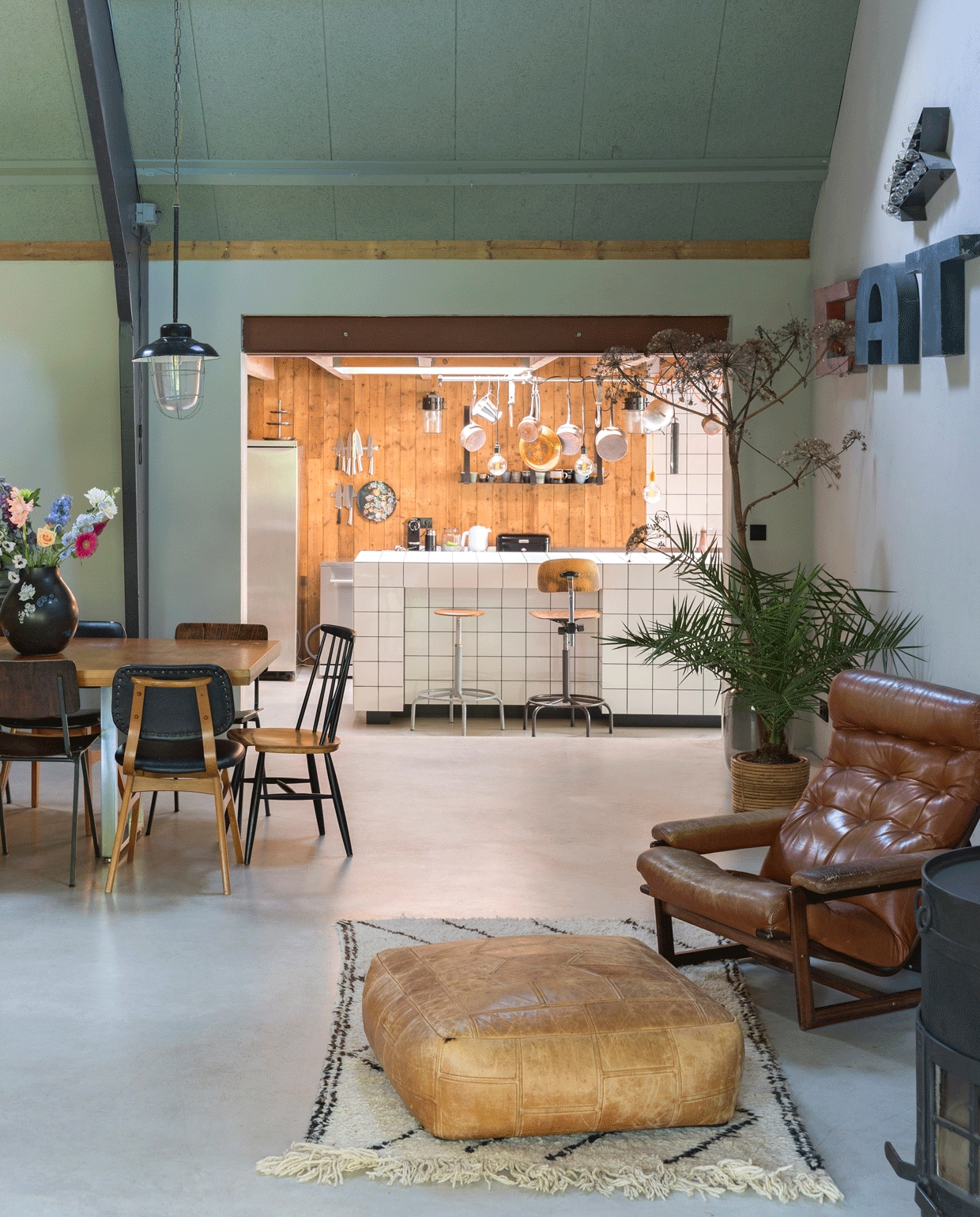 Leren fauteuil van de kringloop, poef gevonden bij de standbouwer waar ook het dakbeschot vandaan komt, kleed uit Marokko, letters EAT van E550, pijl Sissy-Boy, barkruk en -stoel via marktplaats.nl, het keukenblok is zelfgemaakt, erboven pannen van Vivre Interieur Authentique. Hanglamp boven eettafel Vroeger &amp; Toen. Eetkamerstoelen van Montmartre, Davidowski en Tony’s Garage Sale.