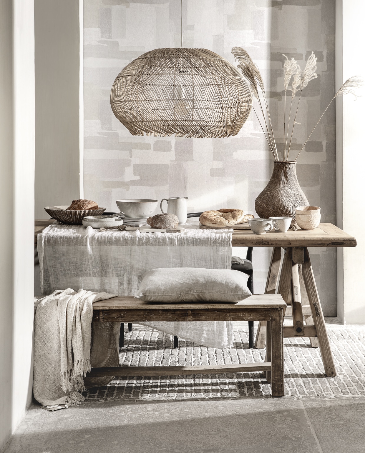 Behang Lino, 106 cm breed (eijffinger.com). Rieten hanglamp (manggisliving.nl). Houten whitewash schaal Marseille (mrsbloom.nl). Servies Broste Copenhagen; schalen, grote schaal, kan, bord, grote kom met oor, bewerkte houten schaaltjes (loftloft.nl). Linnen kussen, eettafel van oud hout, 260×90 cm, oud teakhouten bank 176 cm breed (hetkabinet.nl). Grof geweven plaid (heinshome.nl). Vaas (stylexclusief.nl).