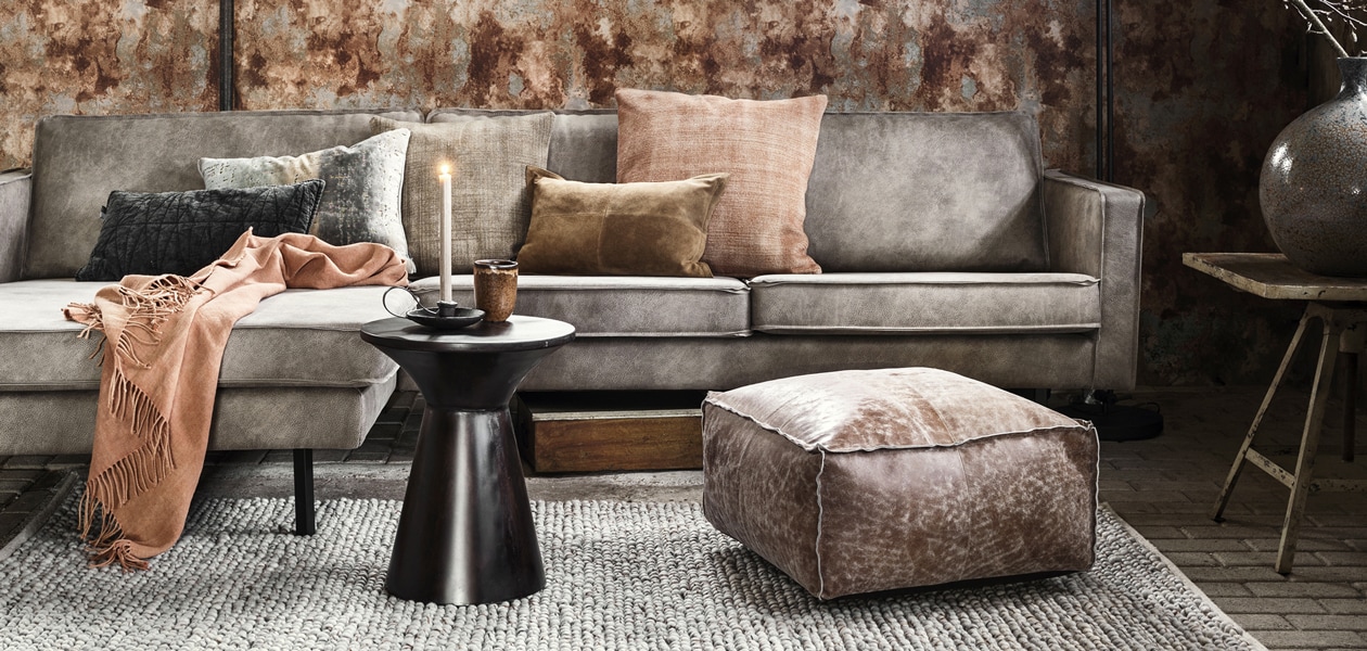 Behang Collection Essentials Design nr. 218005(bnwalls.com). Loungebank Rodeo in Elephant Skin, PU leer en nylon, 300×85 cm (bxh), opdraaitafeltje Repro, kandelaar, oude metalen box (hetkabinet.nl). Stonewashed kussen Lima Copper, 60×60 cm, stonewashed kussen Lima Stone, 50×50 cm, vintage linnen plaid Orange, 140×165 cm (mlfabrics.nl). Suède kussen, antraciet stonewashed velours kussen (heinshome.nl). Velours kussen met steendessin Montmartre Zinc (designersguild.com). Poef met grove leerbewerking Amia, grote keramieken vaas Lynton (intratuin.nl). Zwarte vloerlamp Wesley (light-living.nl). Zwart metalen bijzettafeltje Diaz (karwei.nl). Wollen vloerkleed Cobble 29201 van Brink &amp; Campman, 170×240 cm (vloerkledenwinkel.nl). Bruine aardewerken mok (dille-kamille.nl).