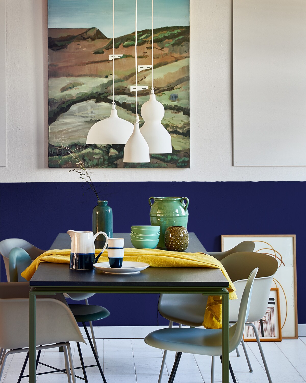 Verfkleur wand boven Chalk White (pure-original.nl). Kleur lambrisering Tai Sapphire 116 (littlegreene.com). Tafel, eetkamerstoelen met zwart onderstel (goeds.nl). Grijze kuipstoelen per stuk, blauw/groene kruik, print op de vloer, eiken lijst (loods5.nl). Ervoor tekening van José Heerkens, aan de wand olieverfschilderij van Margot de Jager (sbk.nl). Lampen van keramiek, groene pot met oren (urbannatureculture.com). Kommen (ikea.nl). Kan, bekers, bord (polspotten.nl). Groen vaasje (fonq.nl). Linnen tafelkleed (weldaad.com).
