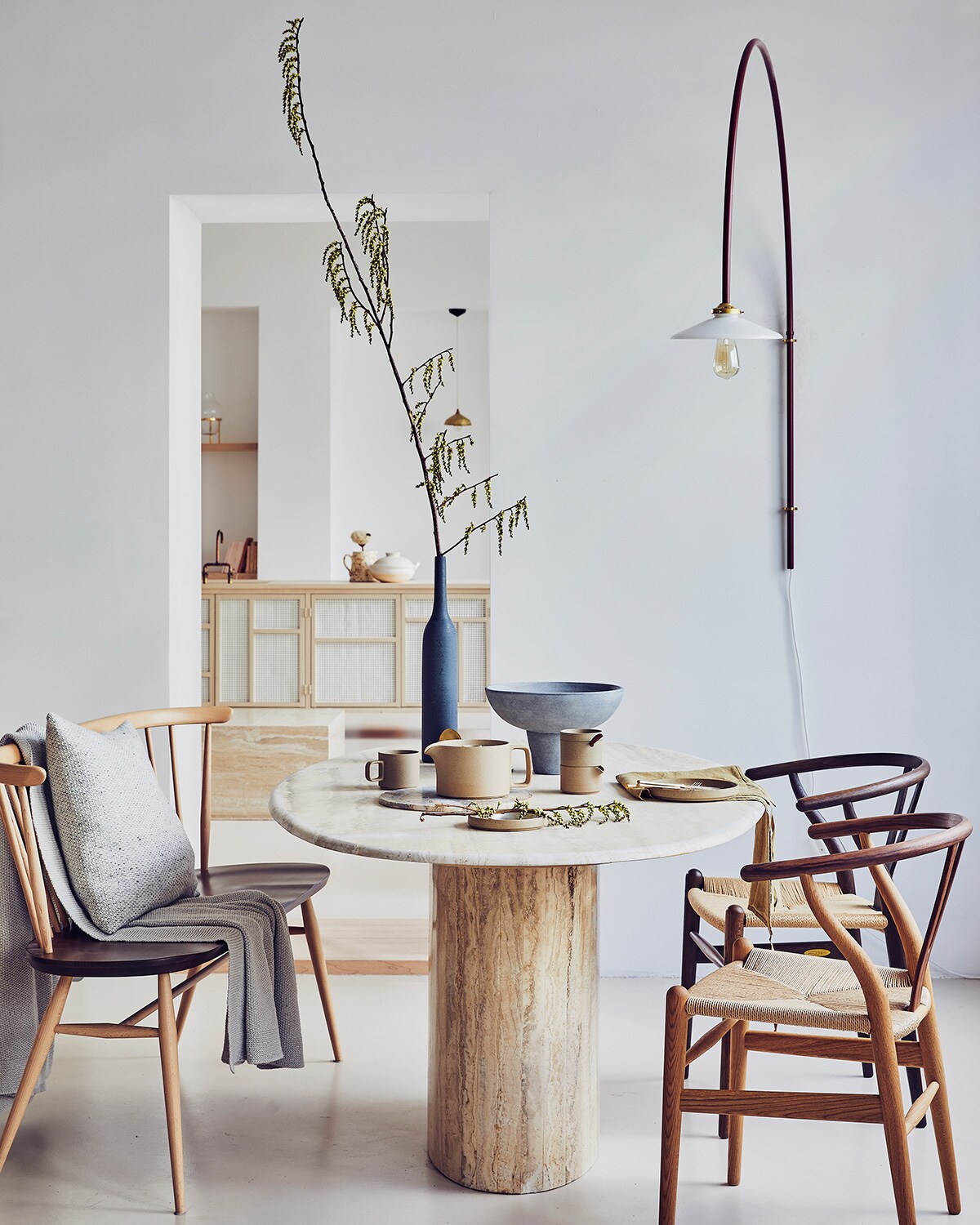 Vintage tafel van travertin, Wishbone chair stoelen van Carl Hansen, van gecertificeerd hout, theepot van Hasami Porcelain, suikerpot en melkkannetje van Hasami Porcelain, bord van Hasami Porcelain, beker van Hasami Porcelain, groene linnen theedoek van Linge Particulier, bankje van Ercol, wollen kussen van Mourne, wandlamp van Muller van Severen (pantoufle-design.nl). Merino wollen plaid (bymolle.com). Grijze schaal op voet (101cph.com). Fles van keramiek (zarahome.com).