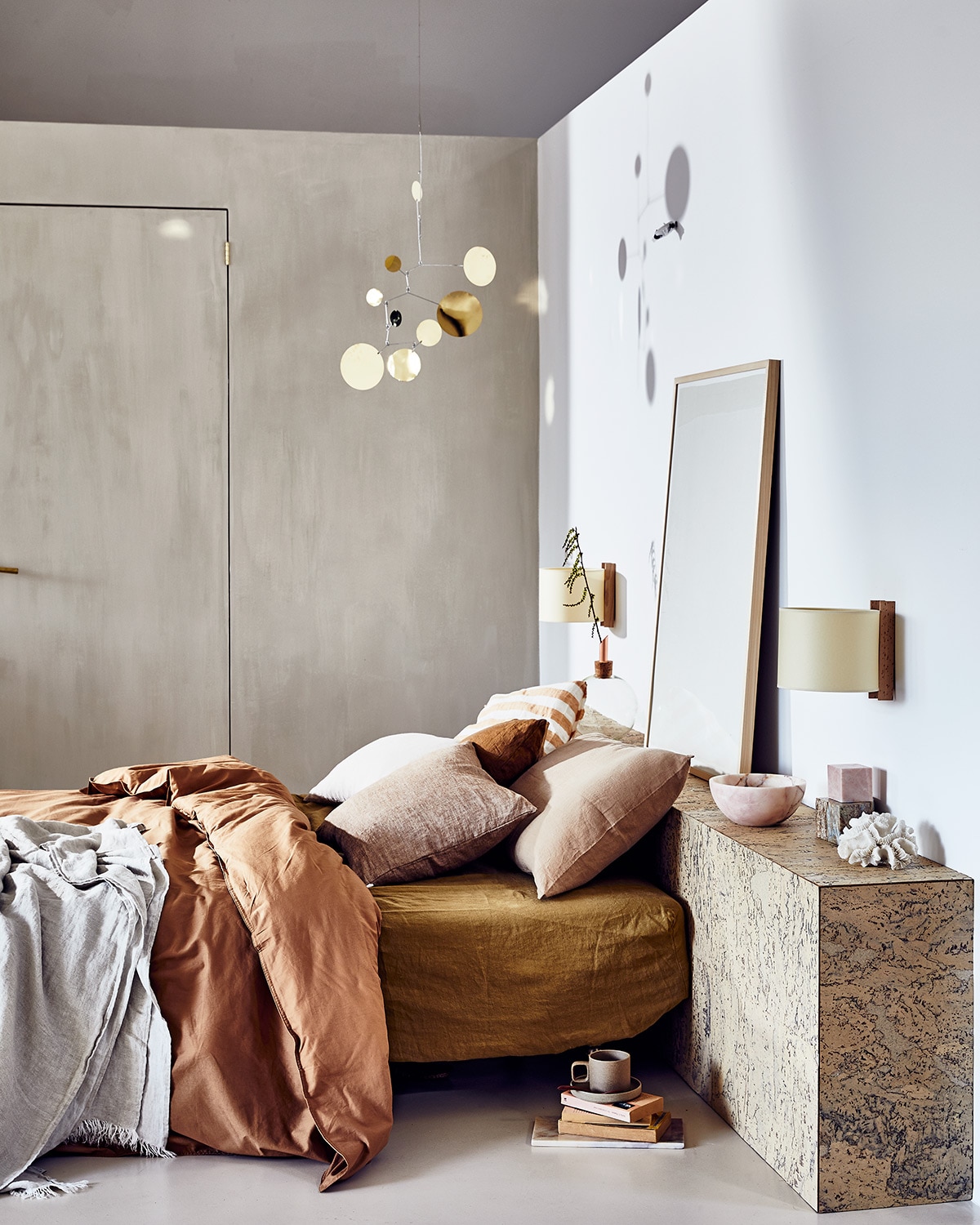 Headboard gemaakt van duurzame kurken wandtegels (24kurk.nl). Messing mobile Lappalainen, wandlampen van Santa &amp; Cole, beker van Hasami Porcelain, beddengoed van biologisch katoen van Midnatt, matrashoes van Linge Particulier, gestreept kussen van Linge Particulier (pantoufle-design.nl). Linnen plaid, linnen kussens Nutmeg, bruin kussen, roze kussen (bymölle.com). Schilderij Fant (sukha.nl). Roze marmeren schaal, marmeren kubussen (stonedmarble.com). Fresco kalkverf op de muur in kleur Coffee Cream (pure-original.nl). Koraal privébezit.