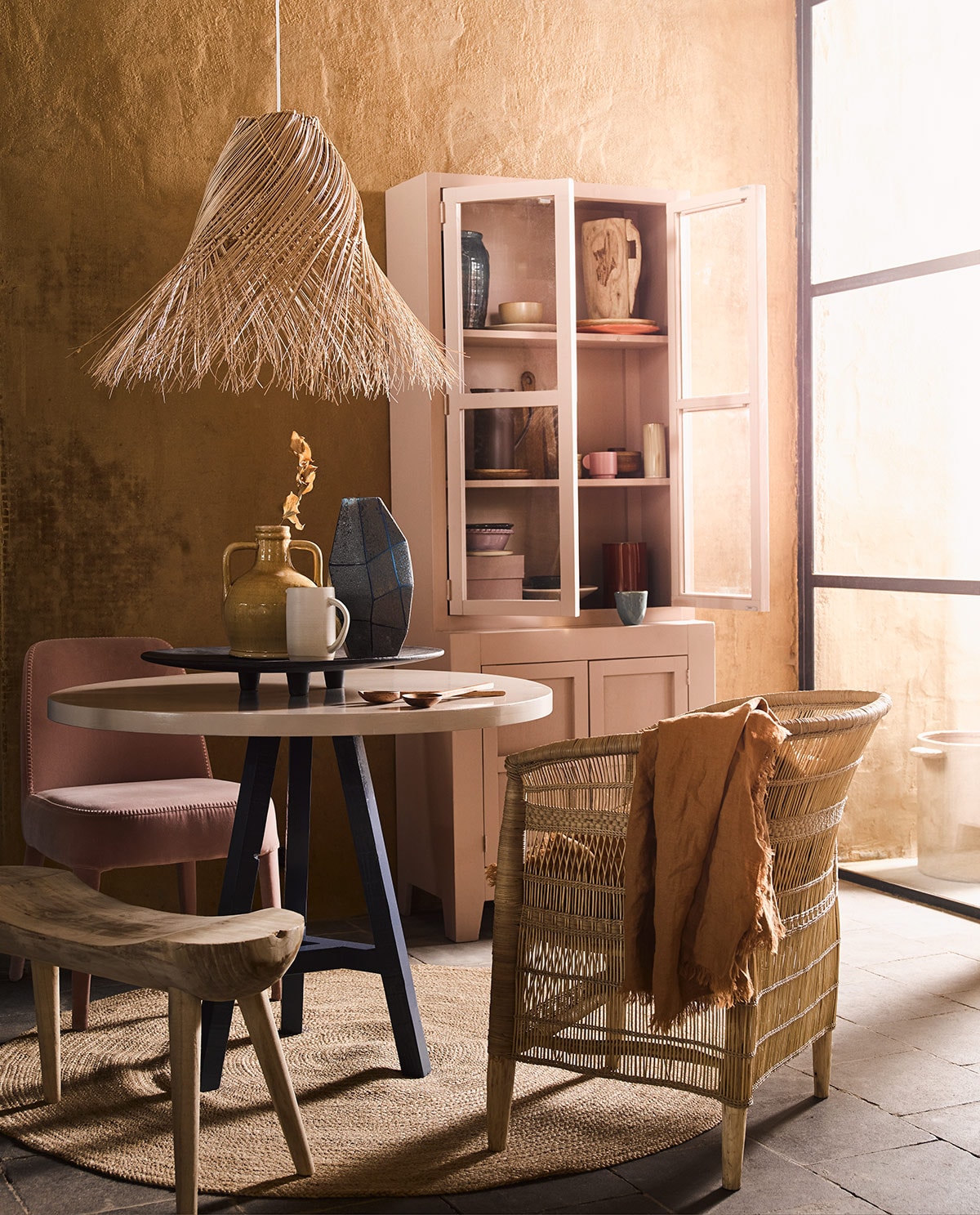 Ronde tafel met blauwe poot, roze kast (com-anders.nl). Hanglamp, gele vaas met oren, rond vloerkleed maat L, zwart dienblad, roze doos in kast, houten bord in kast, oranje bord in kast, bruin bord in kast, geel schaaltje, blauwe vaas linksboven in kast (loods5.nl). Bruin tafelkleed, snijplank, paarse kan, slabestek, bruin potje met deksel in kast, roze mok in kast (hm.com). Blauwe mok, blauwe vaas op tafel (thingsilikethingsilove.com). Roze schaal op poot van HK Living (wonenmetlef.nl). Houten vaas in kast, paars schaaltje in kast links onder, lila schaaltje onder in kast (householdhardware.nl). Pot buiten, rode vaas in kast, beige vaas in kast middelste plank rechts (serax.com). Witte kan op tafel (annemiekebootsceramics.nl). Houten bankje van Mica links (vtwonen.nl). Roze stoel van stof (edha-interieur.nl). Stoel gevlochten hout (archive-store.nl).