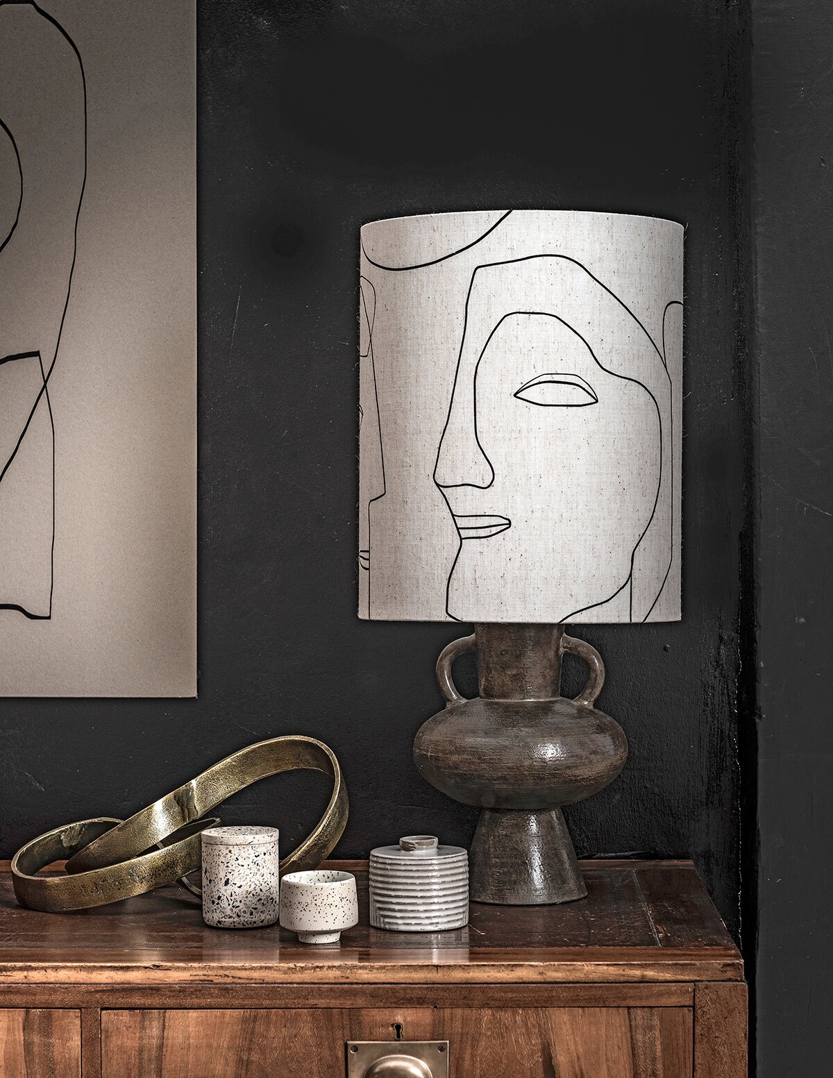 Abstracte inktlijntekening Sola van Henri &amp; Lydia, abstracte inkttekening van Henri &amp; Lydia, handgemaakte printable art van Miuus Studio set van 2(etsy.com). Schaal met lijnenspel, lamp Replica Serge Mouille, leren vlinderstoel voor Airborne, teakhouten dressoir William Watting 19605 (cocooncollectables.nl). Terrazzo vaas van Zakkia (restored.nl). Zwarte bloempot van papier, wit keramiek vaasje met zwarte spikkels (storewithoutahome.nl). Witte vaas Outline (housedoctor.com). Handgemaakte boekensteunen van versteend hout (studiosomee.com). Vloerkleed Desert Tufted Rug Sand (fermliving.com). Boeken en blouse privébezit.