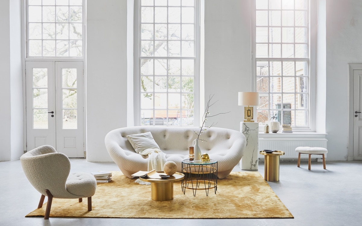 van . 4-zitsbank Ploum van Ligne Roset, okergeel vloerkleed, goudkleurige bijzettafels (misterdesign.nl). Fauteuil Little Petra van &amp; Tradition (mobilia.nl). Bijzettafel met glas en metaal, lamp van messing met zijden kap (paullelieveld.com). Marmeren pilaar, voetenbankje Pebble (polspotten.nl). Linnen plaid, okergele vaas (nordal.eu). Grijze fluwelen kussen, vaas met bladdessin (madamstoltz.dk). Overige privébezit.