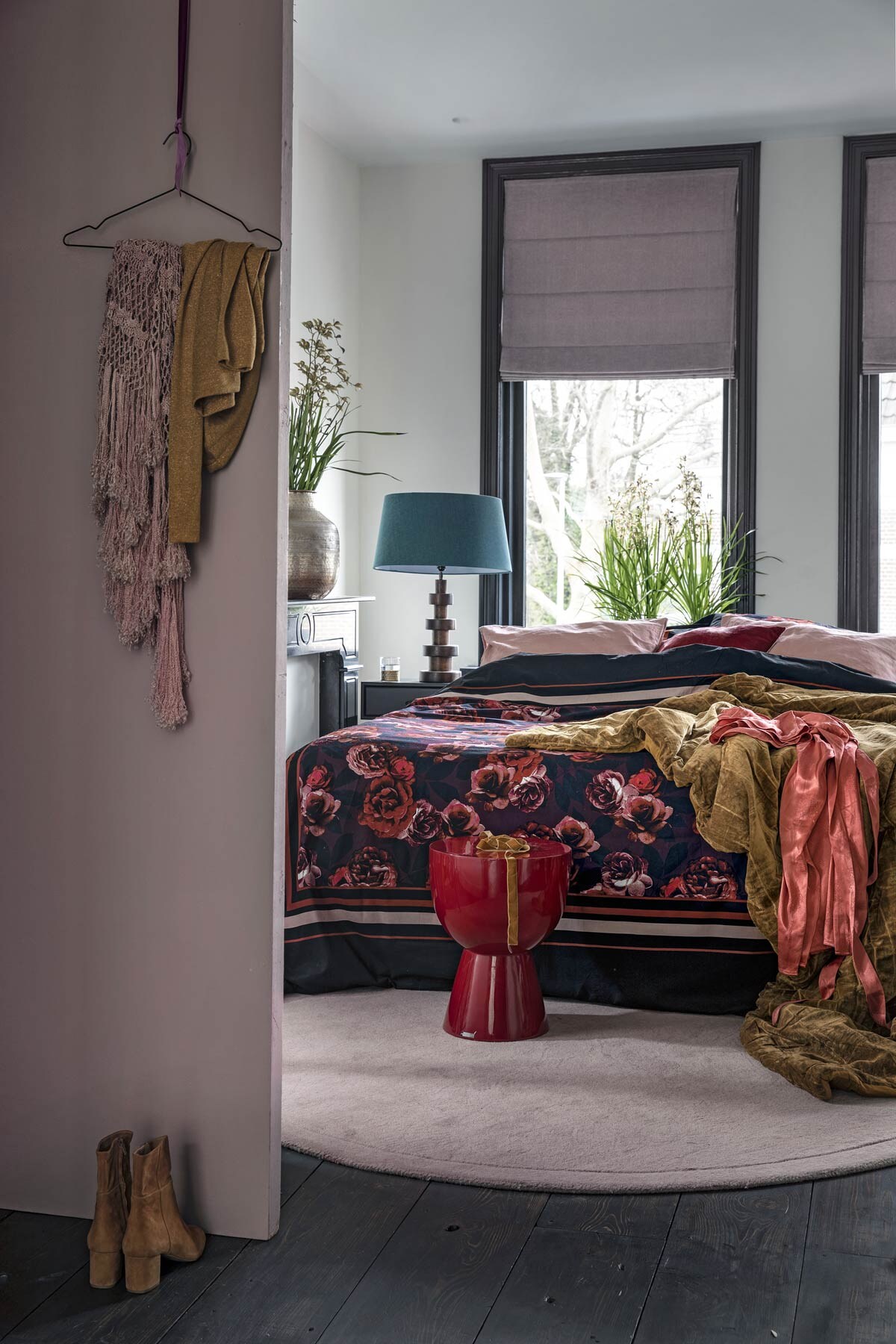 Donkerrood bijzettafeltje Ruby van Pols Potten van vtwonen.nl. Muurverf Sulking Room Pink (Farrow &amp; Ball). Dekbedovertrek met rozendessin, poederroze kussenhoezen, rood-roze kussen Dores van Casa Vivante, roze satijnen jurk (hm.com). Okergele velours sprei (hkliving.com). Grote messingkleurige vaas, tafellamp met houten voet (hetkabinet.nl). Rond vloerkleed Edge in Alpine Rosa (sofacompany.com). Overig privébezit. vtwonen 02-2019 | styling Moniek Visser  | fotografie Peggy Janssen