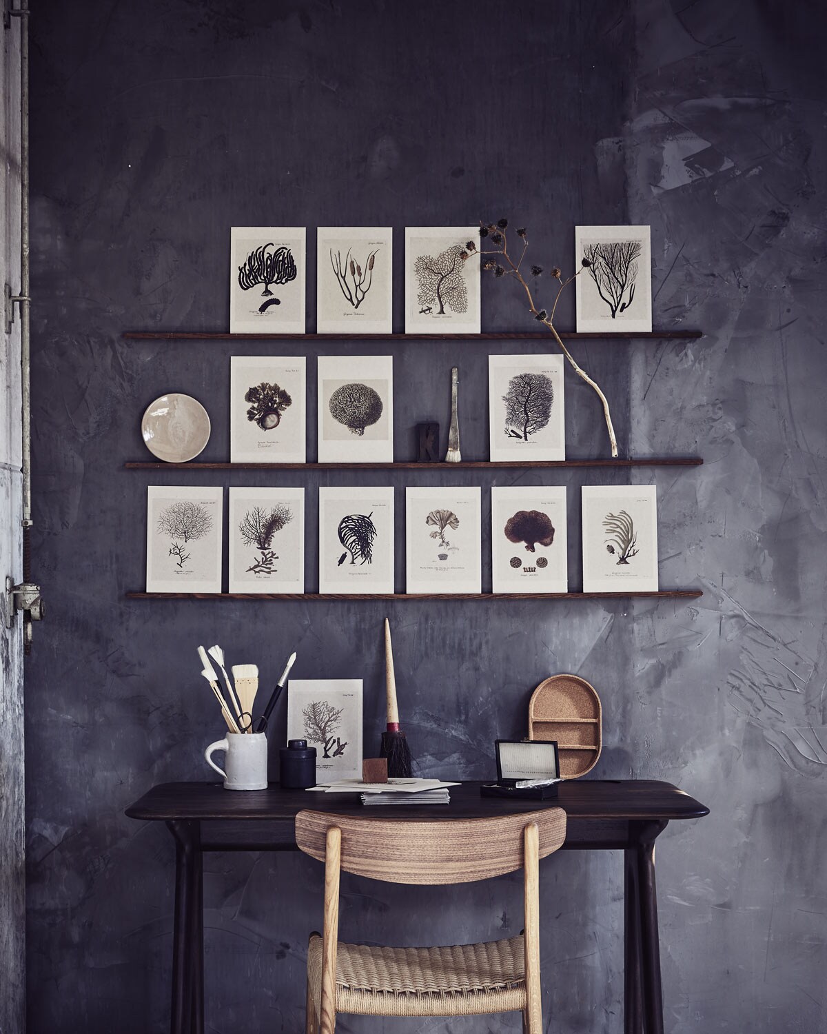 Kartonnen kaarten met print gemaakt bij de kopieerwinkel (). Bureau Slab Desk van Tom Dixon, stoel CH23 walnoot van Carl Hansen (). Bordje (). Zwart metalen potje met deksel (). Oude kwasten (). Houten doosje (). Penselen (). Beker (). Kurken bakje Saxborga (). Muur is gestuukt met Marakech Walls van Pure &amp; Original in kleur Thunder Sky, 2,5 liter ().