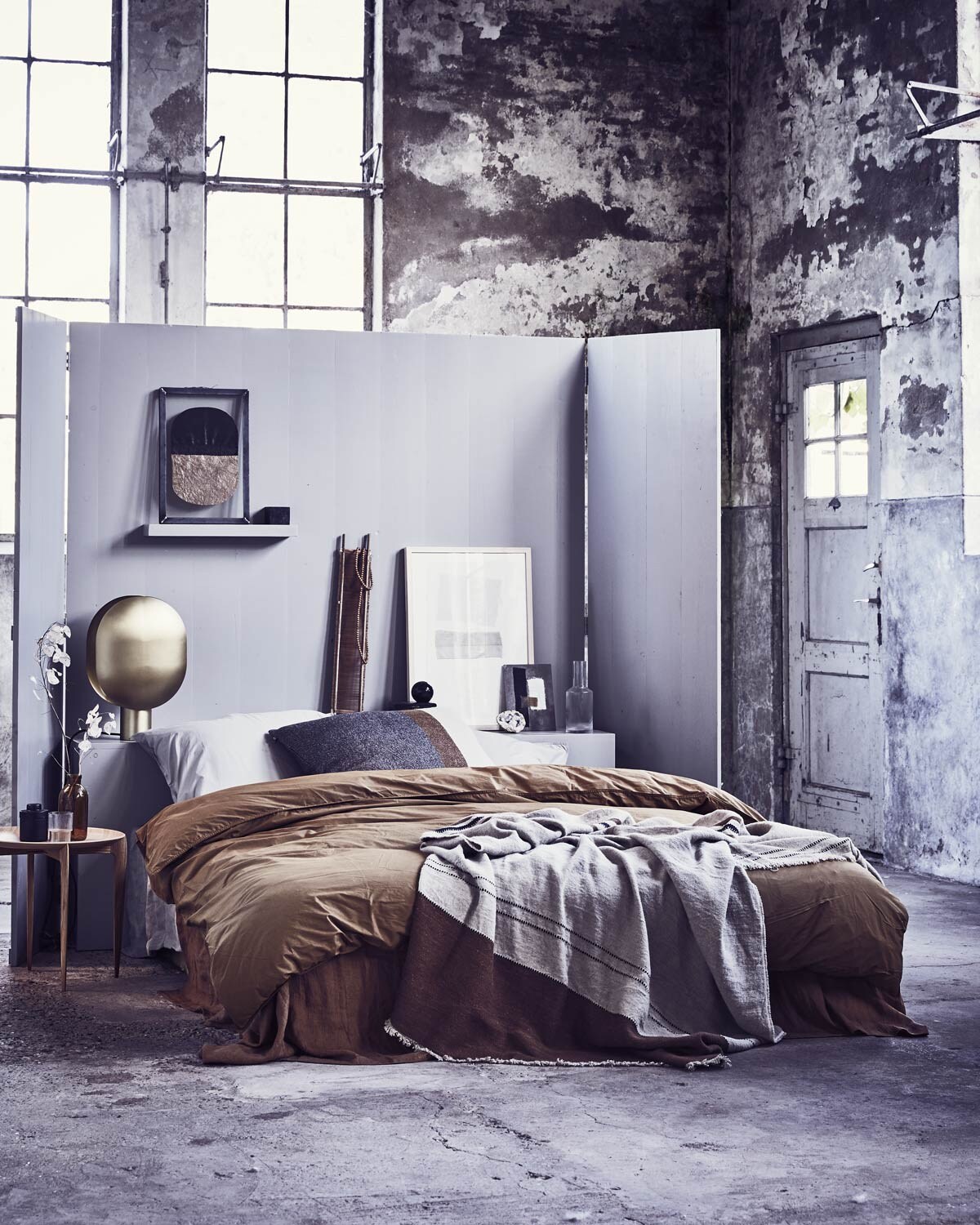 Headboard/kamerscherm, op maat gemaakt (). Grote lijst met ingelijste textielkunst van Fant, klein kunstwerk op karton van Birgitta de Vos, houten ketting (). Kunstwerk in stalen frame met papier van Laura de Wilde X Lola Kate 03 (). Gestreepte sprei van Libeco van linnen en wol, bruin gestreept kussen (. Linnen laken, kaneelkleur (). Dekbedovertrek perkal katoen, kaki-goud zonder kussenslopen, kussenslopen zilvergrijs (). Glazen karaf, glas van Ferm Living, zwart potje met deksel (). Salontafel Tray Table van Fritz Hansen (). Messing lamp Clamp van Norr11 (). Smalle houten zeef (). Overig privébezit.