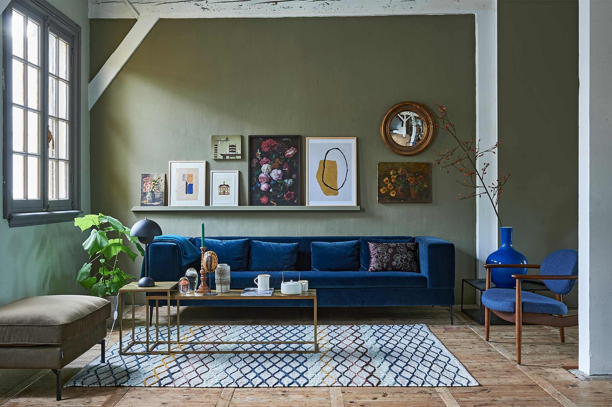 Op de wand muurverf Classico in kleur Tundra (). Bank van blauw velvet, lampje op salontafel (). Salontafel brass, stoel met houten frame, grote blauwe vaas, poef, geborduurd kussen op de bank (). Zwarte metalen bijzettafel, retro vaas, glazen kwallen, namaak schildpad, theepot (hkliving.nl). Kom, kan, rozenbotteltak XL (). Vloerkleed (). Op de wandlijst: v.l.n.r. schilderij met bloemen (privébezit), grafisch werk (), illustratie gemeentehuis van Michiel van der Zanden (), erboven stoel + tafel (privébezit), print bloemen van het Rijksmuseum (), in lijst Hovsta (), grafisch werk (), bloemenschilderij (privébezit). Goudkleurige oude spiegel ().