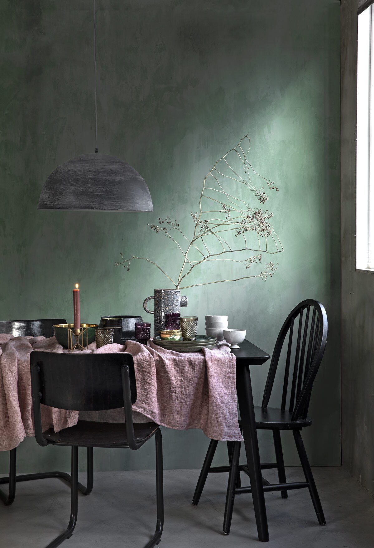 Wand is geverfd met kalkverf in de kleur Lagune (). Zwarte eettafel Lisabo (). Betonlook  Lucide Mattie, groene  Bitz Born (). Grijze kruikvaas, witte kommetjes, blauwe-grijze schaal Grey Stone (). Auberginekleurige wijnglazen, champagnekleurige glazen Diamond (). Goudkleurige schaaltjes, schaal met groen met goudkleurige binnenkant, kandelaar, roze dinerkaars ().  Pink Salt van By Mölle (). Stoelen privébezit.