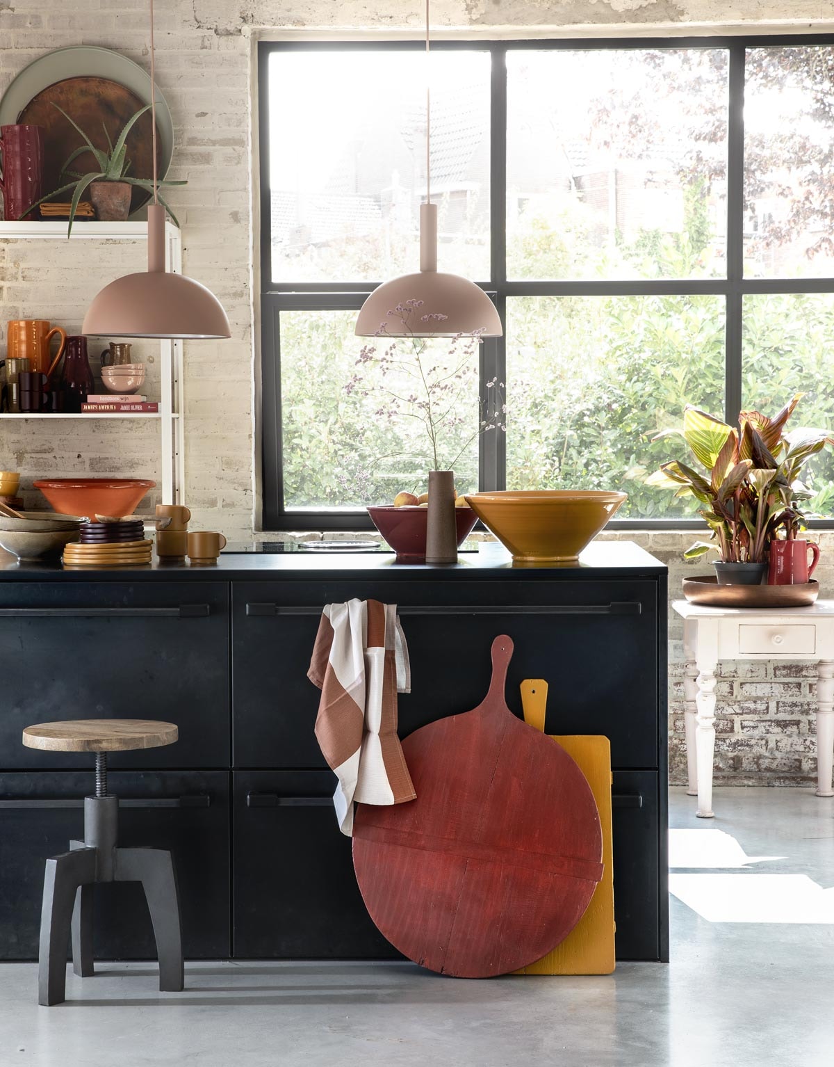 Zachtroze hanglampen Dome Shade van Ferm Living inclusief roze fitting High (vtwonen.nl). Draaikruk Space van BepureHome (Woondock). Grote oude kaasplanken (H&amp;M Home), gelakt met Perfection zijdeglans lak in dieprood en mosterdgeel (Histor). Theedoek, okergele kopjes, okergele borden, donkerpaarse borden (H&amp;M Home). Okergele schaal, donkerrode schaal (In-Petto). Beige schalen (Intratuin). Bovenop de kast: grote donkerrode kan (In-Petto), theedoeken in okergeel en donkerpaars (H&amp;M Home), koperkleurige schaal van BePureHome, zachtgroene schaal (Woondock). Midden in de kast: zachtroze schaaltjes, okergele kan (In-Petto). Donkerpaarse kopjes (H&amp;M Home). Donkerrode karaf Nikki, lichtbruine karaf (Intratuin). Beige kan (Intratuin). Onder in de kast: terracotta schaal, okergele diepe borden (In-Petto). Zachtroze tafeltje (Combitex). Koperkleurige schaal Big Waitress van BePureHome (Woondock). Donkerrode kleine kan (In-Petto). Kamerplanten Canna Hybride (Intratuin). De keuken is een eigen ontwerp van de bewoners, binnenwerk van hout, blad en kasten afgewerkt met blauw staal. Overig privébezit. vtwonen 11-2018 | styling Moniek Visser | fotografie Peggy Janssen