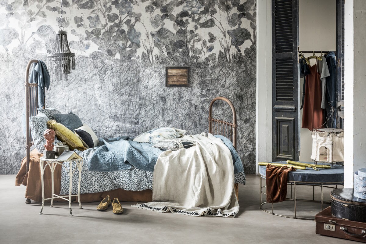 Novilon vloer kleur zand (vtwonen.nl/vtwonen-collectie). Op maat gemaakt behang (Wall and Deco). Bed (Vroeger &amp; Toen). Blauw tafelkleed (Tine K Home). Hanglamp, tentlamp, kunstwerkje aan de muur, gevlekt kussen, zwart-wit kussen, witte plaid met zwarte rand (Brecht Murré Atelier). Blauwe poef (De Weldaad). Koffer, hoedendoos, deuren (Burbri Antiek). Kledinghanger, blauw doosje, blauwe plaid, blauwe kussentjes, doos met print (Zara Home). Kruk als nachtkast (Neef Louis). Gebloemd dekbedovertrek (Ikea). Geel kussen (Loods 5). Borstbeeld (Harlequin Antiek). Notitieboekje (MaisonNL). Bakje met gouden handgreep, fluwelen topje, oranje jurk (Things I Like Things I Love). Wit kussen met blauw vlak van Mica (vtwonen.nl).