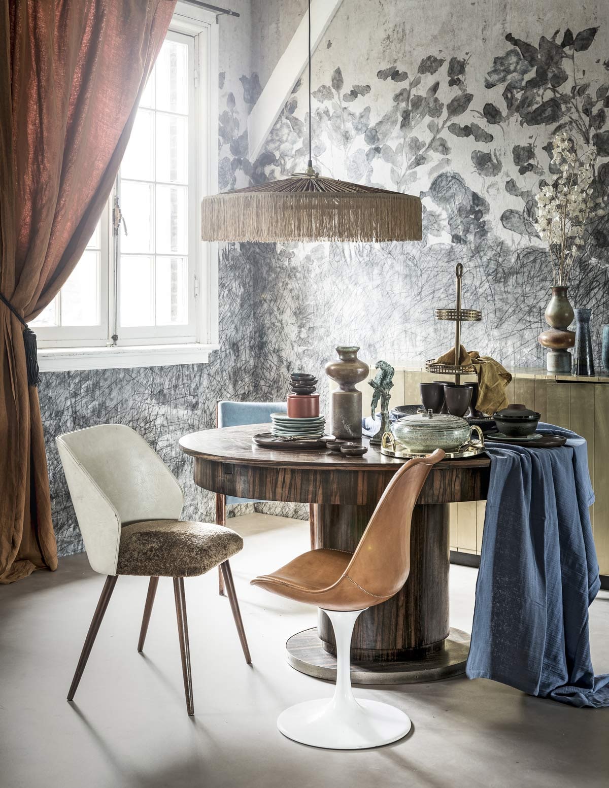 Novilon vloer kleur zand (vtwonen.nl/vtwonen-collectie). Op maat gemaakt behang (Wall and Deco). Linnen gordijn, leren kwast, bruinleren stoel met witte voet (Brecht Murré Atelier). Tafel, blauwe stoel, smalle vaas (Neef Louis). Bruine stoel met witte leuning (Van Dijk &amp; Ko). Hanglamp (MaisonNL). Blauw-oranje vazen met bolle vormen (The Wunderkammer). Gouden kast, etagère gold (Loods 5). Blauwe borden van HKliving, bruin potje met deksel van Madam Stoltz, grote blauwe schaal van Casa Vivante (vtwonen.nl). Geel servet, oranje bakje (H&amp;M). Gouden schaal (Zara Home). Vogelbeeldje (Harlequin Antiek). Tafelkleed, bruine beker, bruine borden, bruine kommetjes (Tine K Home). Blauwe schaal met deksel (Things I Like Things I Love). Gouden bestek (Anna+Nina).
