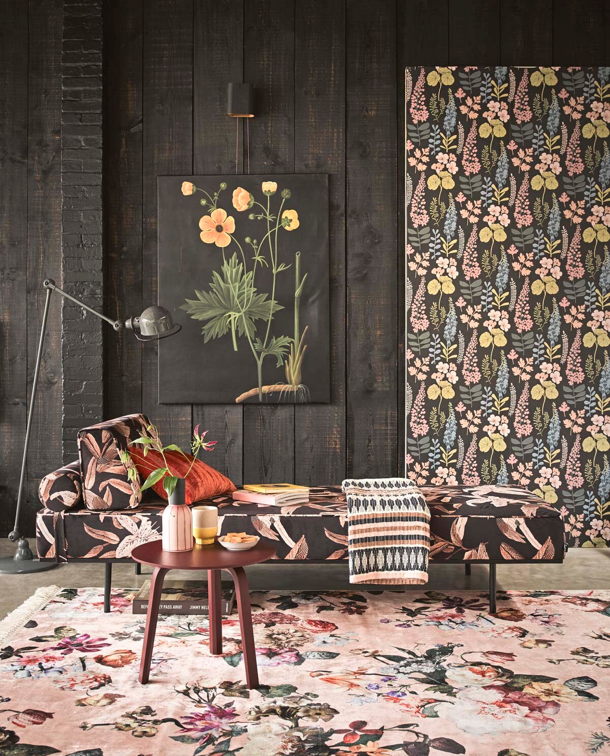 Behang Vivid met bloemenprint (Eijffinger). Velours daybed, veelkleurige plaid (HKliving). Vloerkleed met bloemenprint (Essenza Home). Steenrood tafeltje (Hay). Schilderij bloem (Pols Potten). Staande lamp Jieldé (Fens Decor). Oranje kussen Amelie Poppy William Yeoward (Wilhelmine van Aerssen). Vaas met roze streep (Loods 5). Beker met gele voet (Return to Sender).