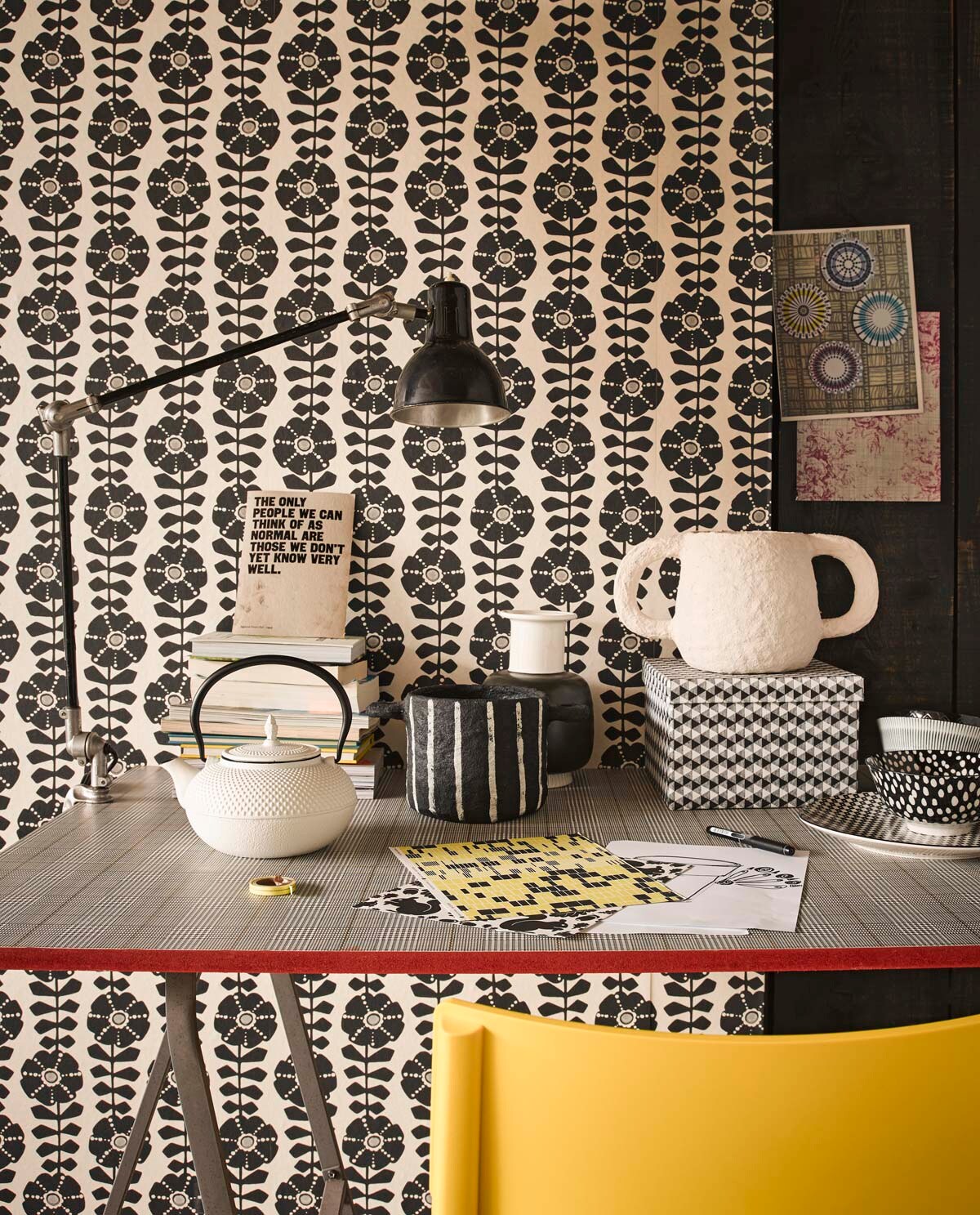 Behang Black &amp; Light met grafische bloemenprint, tafelblad beplakt met behang Atlantic (Eijffinger). Gele kunststof stoel, schragen (Ikea). Zwarte bureaulamp (Neef Louis). Witte Japanse theepot, zwart-witte pot papier-maché, witte pot met oren, vaas zwart-wit, doos, bord, kom zwart-witte stip, beker met streep (Loods 5).