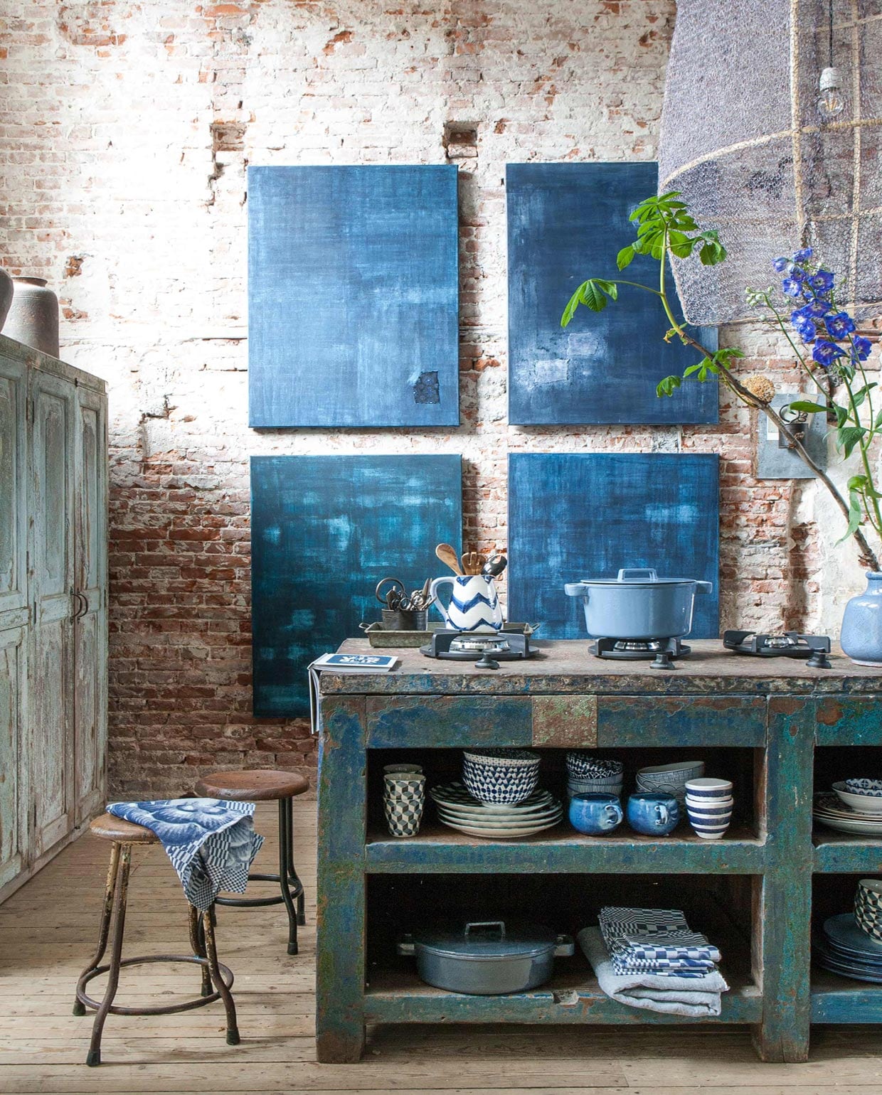 Werkbank, schilderijen van , indigo pigment op linnen canvas, kast, potten op kast, krukjes, lamp van , aluminium potje, blikken dienblad, pollepels per set van twee (). Industriële kookpitten prijs op aanvraag (). Mokken met blokmotief per vier (). Pannen van gietijzer, schenkkan met zigzagmotief, vaas, theedoeken van Hollandsche Waaren per stuk, linnen doek, overige servies (). vtwonen 10-2016 | Fotografie Anna de Leeuw | Styling Marianne Luning