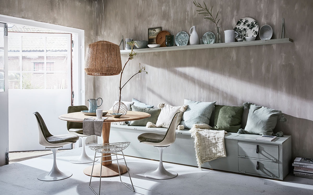 Klepbank op maat gemaakt, lange wandplank (Combitex). Rond dienblad Blossom Leaves van Urban Nature Culture, groen linnen kussen Jade Moss van By Mölle, linnen kussen Jade Green van By Mölle (vtwonen.nl). Emaillen bord groen met wit, diep bord groen/wit emaille, emaillen schaaltje op tafel groen/wit (Hay Amsterdam). Ronde tafel van beukenhout (De Machinekamer). Lampenkap van jute (Nordal). Ecru kussenhoezen met kwasten, groen kussen (H&amp;M Home). Witte kan met reliëf, glazen vaas met jute vlechtwerk, groene glazen, linnen plaid (De Weldaad). Vintage tulpstoelen van Spoor 38 (Vint. Amersfoort). Witte vintage kruk van Pastoe (Neef Louis). Keramieken kan, ovale schaal op tafel, witte beker, grote groene schaal op plank, lichtgrijze kan, ronde houten schaal (Kitchen Trend Products).De bank en plank zijn geschilderd in de kleur Blue Grey van Farrow &amp; Ball (De Ru). De muur is geschilderd in de kleuren Egg White en Light Grey van vtwonen (Karwei).