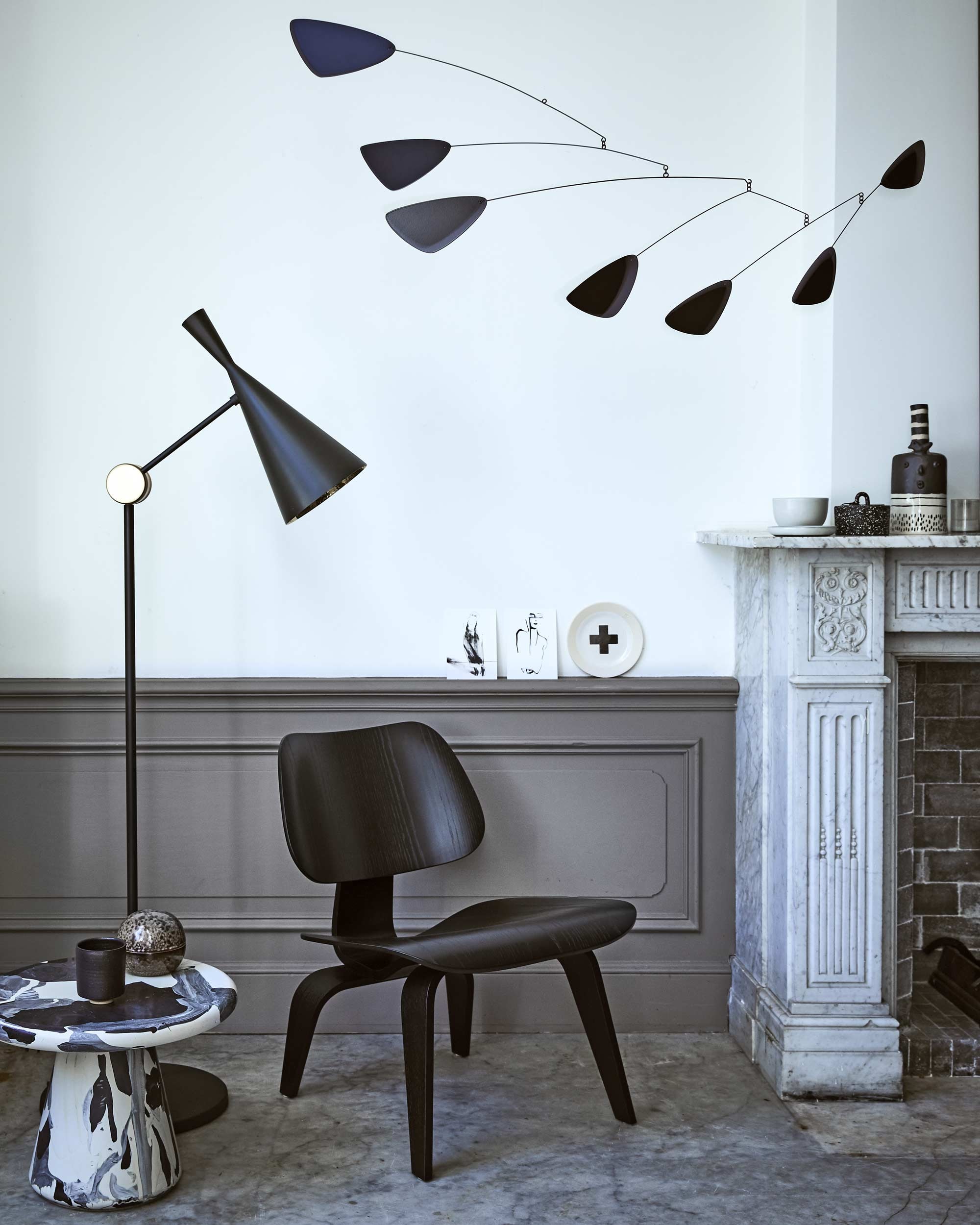 Mobile van Volta, staande lamp Beat van Tom Dixon, zwarte fauteuil Plywood Group LCW van Eames (). Bordje met kruis van Marga Janssen (). Zwart-witte vaas (). Kaarten van Petra Lunenburg, kom, klein schaaltje (). Zwart bakje met stippen en deksel van Ferm Living, bruin bolvormig bakje, zwart potje met deksel (). Bijzettafel Melting Pot van Dirk Vander Kooij ().