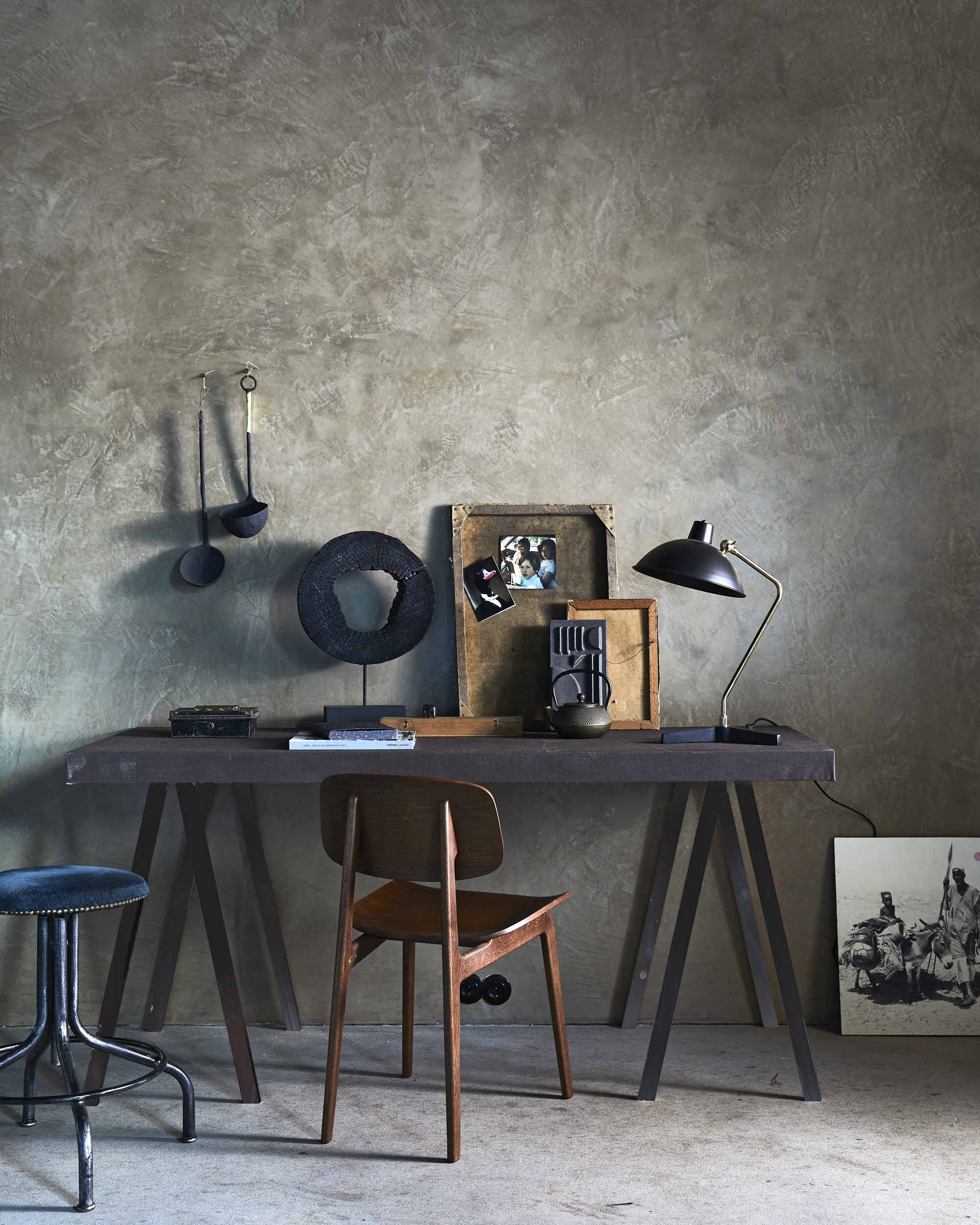 Tafelblad van underlayment, omspannen met schilderslinnen (Jakob Nijsen), geverfd met bruine latex (KARWEI). Walnoot-houten stoel, koperkleurige, gietijzeren theepot (Loods 5). Lamp (Dutchbone). Zwart ornament (HKliving). Foto op de grond (Van Dijk &amp; Ko). Lepels van papier-maché (Mirjam Franken). Keramisch muurornament, set van 3 (House Doctor). Kruk, schragen en bakje privébezit.