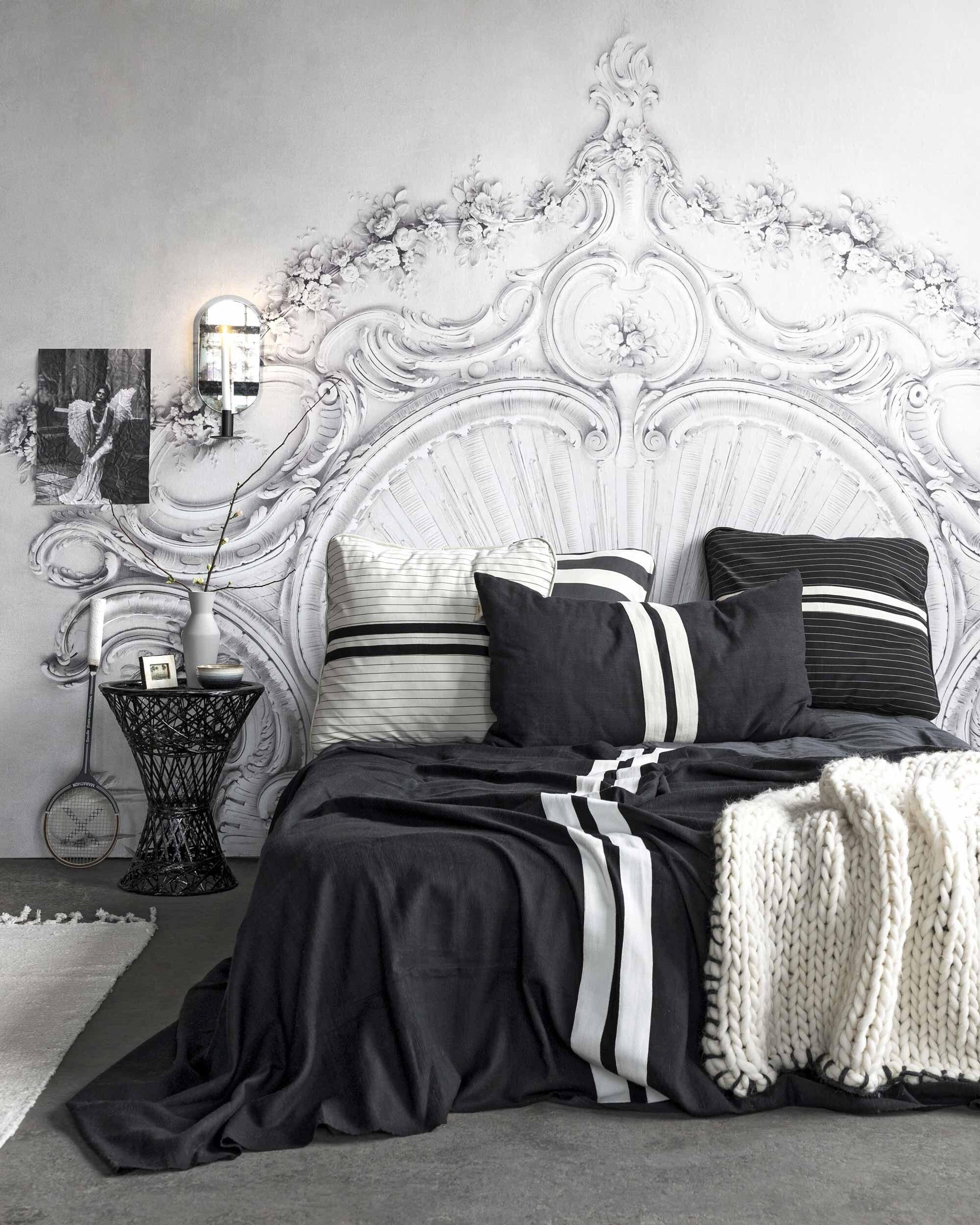 Behang Stucco Gloria van Rebel Walls (De Ru). Zwarte sprei met witte strepen, gestreepte kussens van jersey, vierkant, rechthoekig (10Days). Gebreide plaid met zwarte rand, kom, fotolijst (HKliving). Tafel (Household Hardware). Vaas van Ferm Living, kaarsenstandaard met spiegel van Ferm Living (Kolk en Kolk). Vloerkleed van vtwonen (vtwonen).
