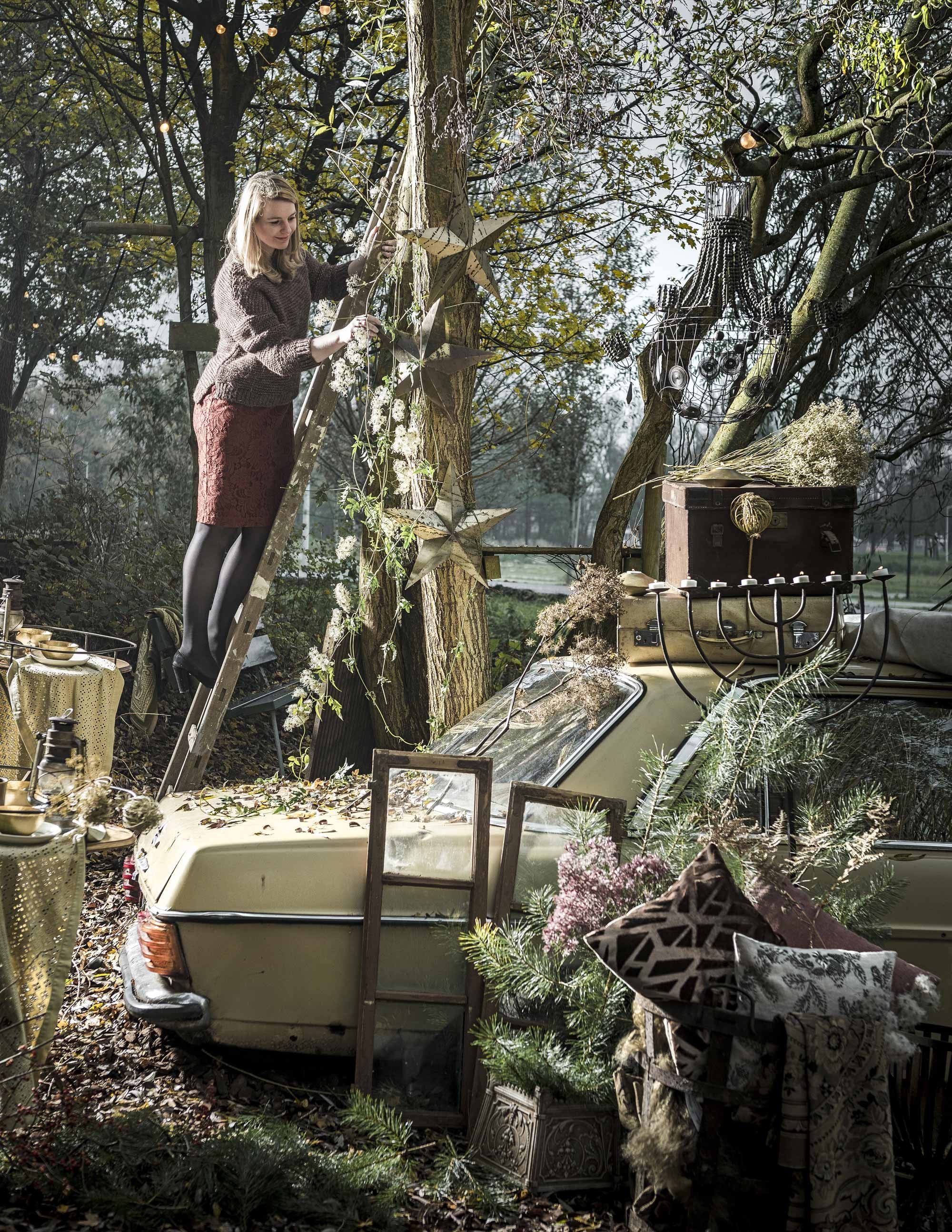 Rood jurkje (H&amp;M). Dikke rode trui (MaisonNL). Sterren, borden, goudkleurige kaarsenstandaard (Anna+Nina). Roestkleurige lamp, kussen met vacht (Brecht Murré Atelier). Goudkleurige bakjes, lopers, roestkleurig kussen met print, kussen met bloemenprint (Zara Home). Set ramen, kleed in mand en op bankje, mand (Van Dijk &amp; Ko). Stalen plantenbak (De Weldaad). Kaarsenstandaard, bruine koffer, grote witte koffer (Burbri Antiek). Oud-roze linnen kussen (Raw Materials).