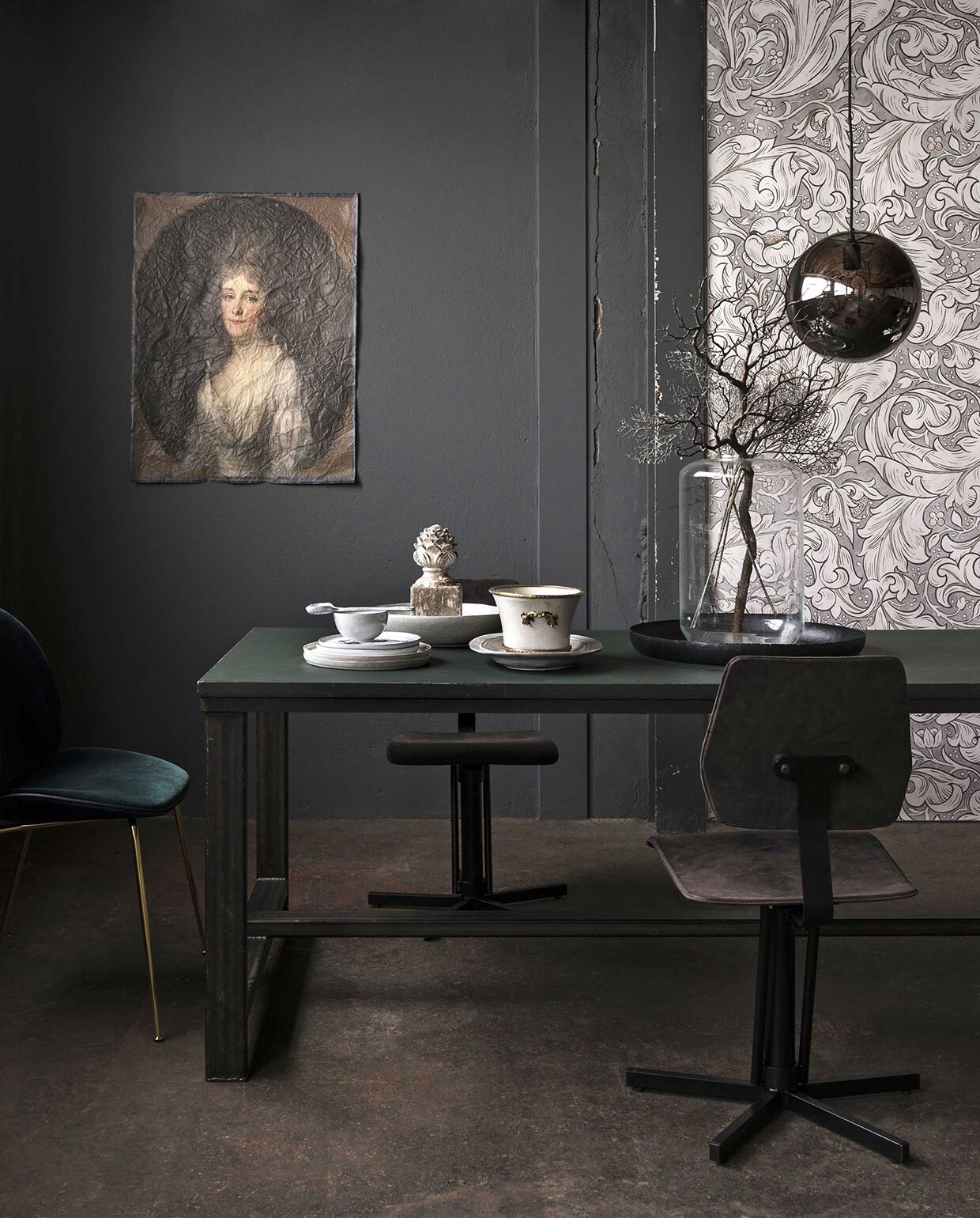 Op de muur muurverf kleur Scree van Little Greene, behang van William Morris by stylelibrary.com, Sanderson Bachelors Button 216050 (). Tafel met stalen frame en marmoleum bovenblad (). Dining chair van Gubi bekleed met fluweel (). Industriële stoel van staal en leer (). Wanddoek uit het Rijksmuseum Archief (). Hanglamp, glazen vaas, kunststof takken, borden, bestek van keramiek, kommetje, serveerschalen, ornament (). Zwart dienblad van vtwonen (vtwonen.nl/vtwonen-collectie). Schaal met goudkleurige afwerking (). vtwonen 13-2017 | Fotografie Stan Koolen | Styling Marianne Luning
