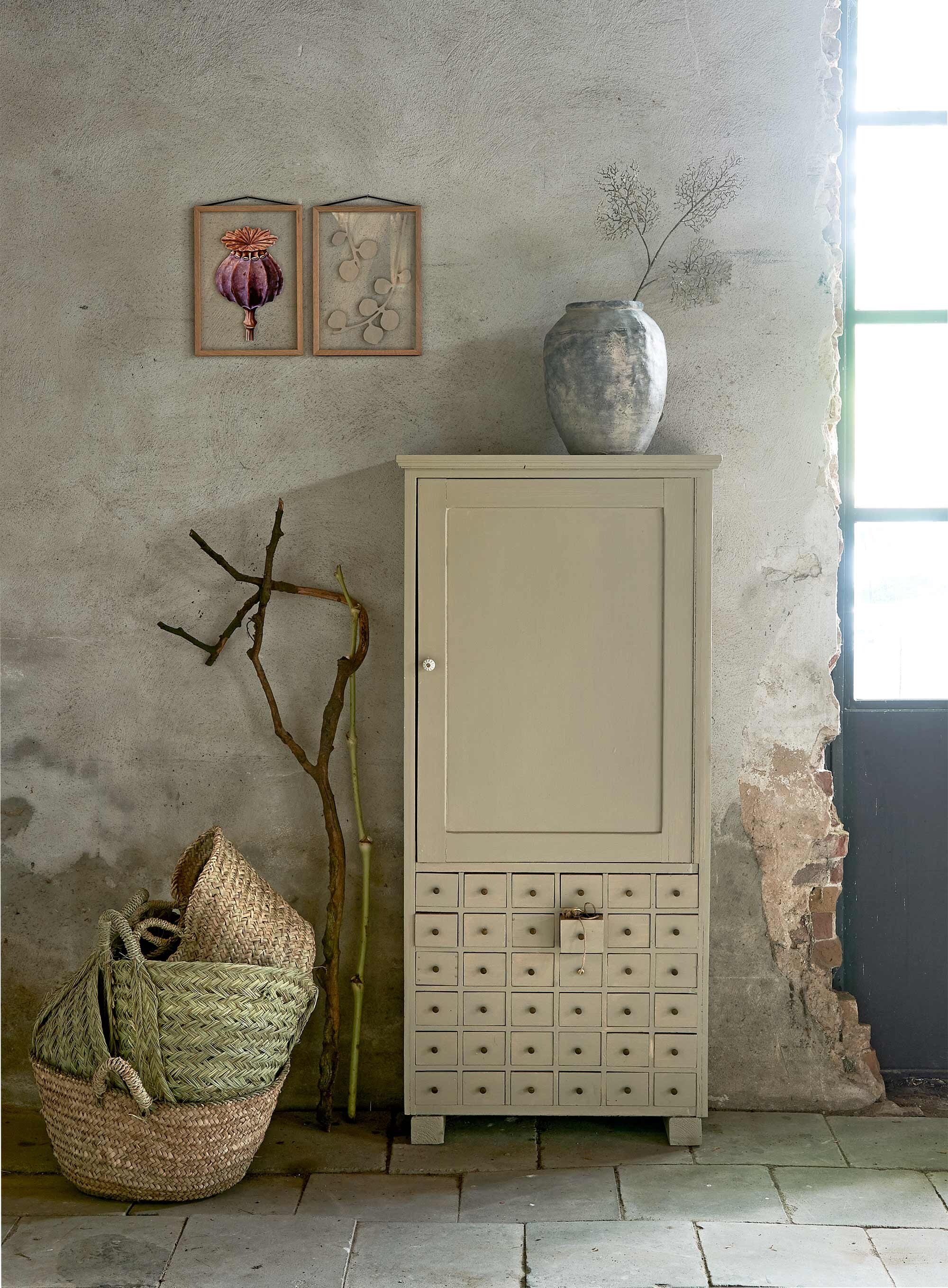 Lichtgrijze kast met laatjes (Burbri Antiek). Betonnen pot, kunsttak (HKliving). Lijst (Moebe). Rotan manden (Household Hardware).