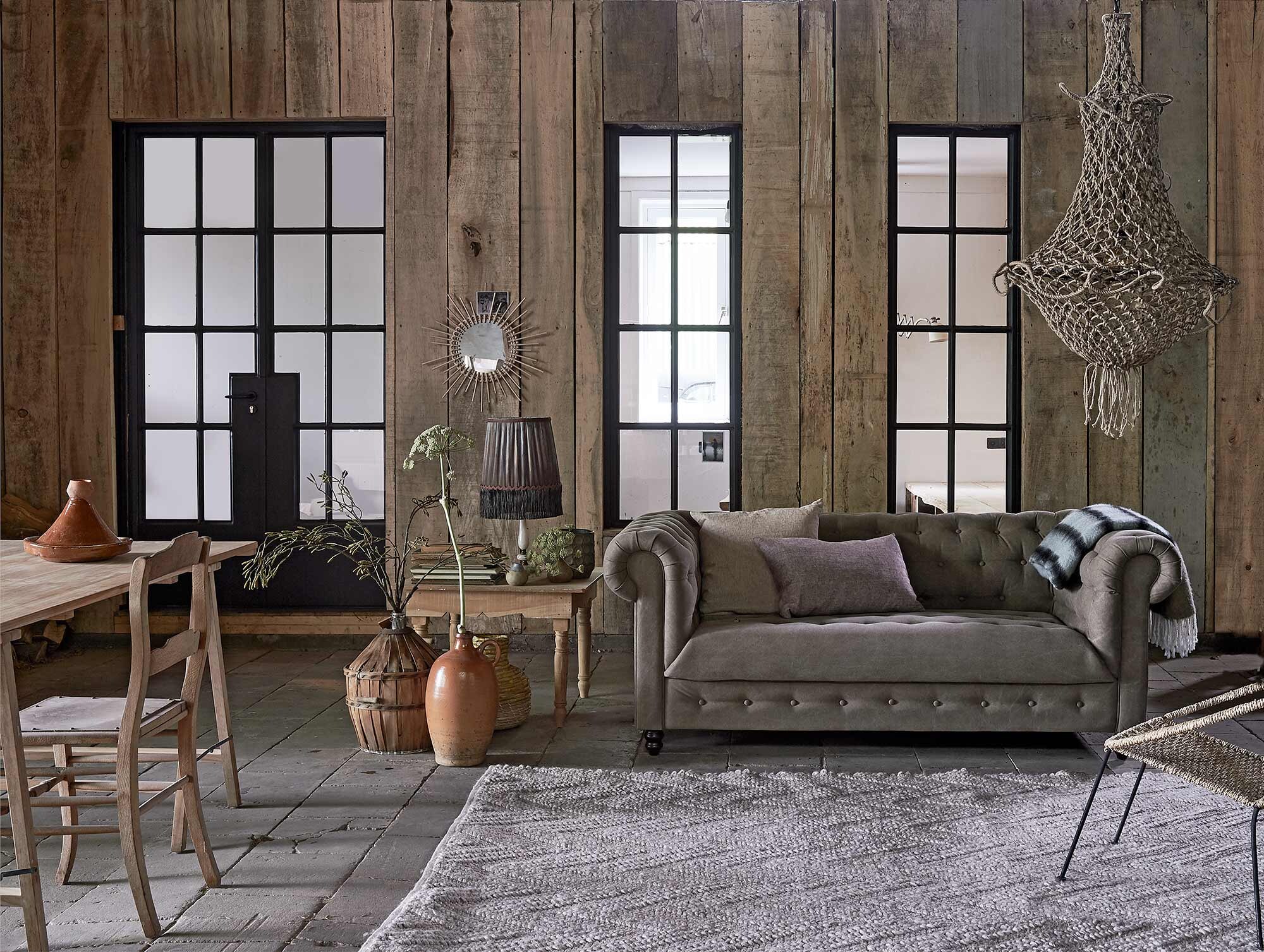 Bank Chester (Dutchbone). Kussen van By Mölle (Nijhof). Karpet Punja (Zuiver). Houten salontafel (Household Hardware).Vintage schemerlamp (MaisonNL). Donkere vaas met cirkeldessin, vaasje met blauwe rand, kunsttak in gistfles, schragentafel (HKliving). Stenen kruik, gistfles met riet, houten stoel (Burbri Antiek). Rotan vaas (IKEA). Tajine, rotan spiegel Soleil (Household Hardware).